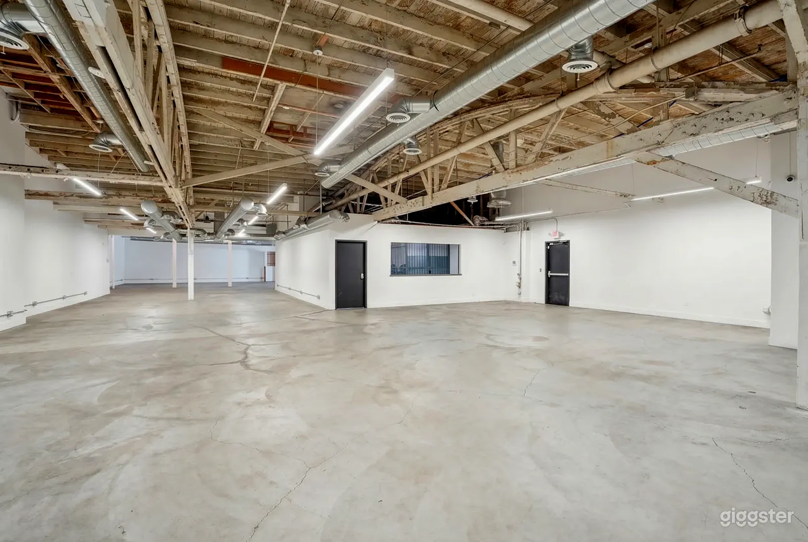 An empty garage space has a cement floor, white walls and industrial type pipes on the ceiling.