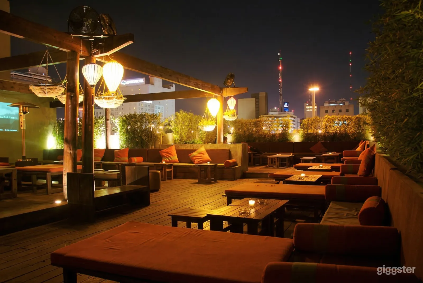 A softly lit rooftop terrace has multiple seating arrangements of benches and loungers under stylish lamps.