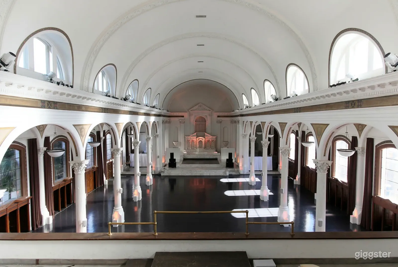 A large room painted white with dark floors has multiple ornate columns lining either side.