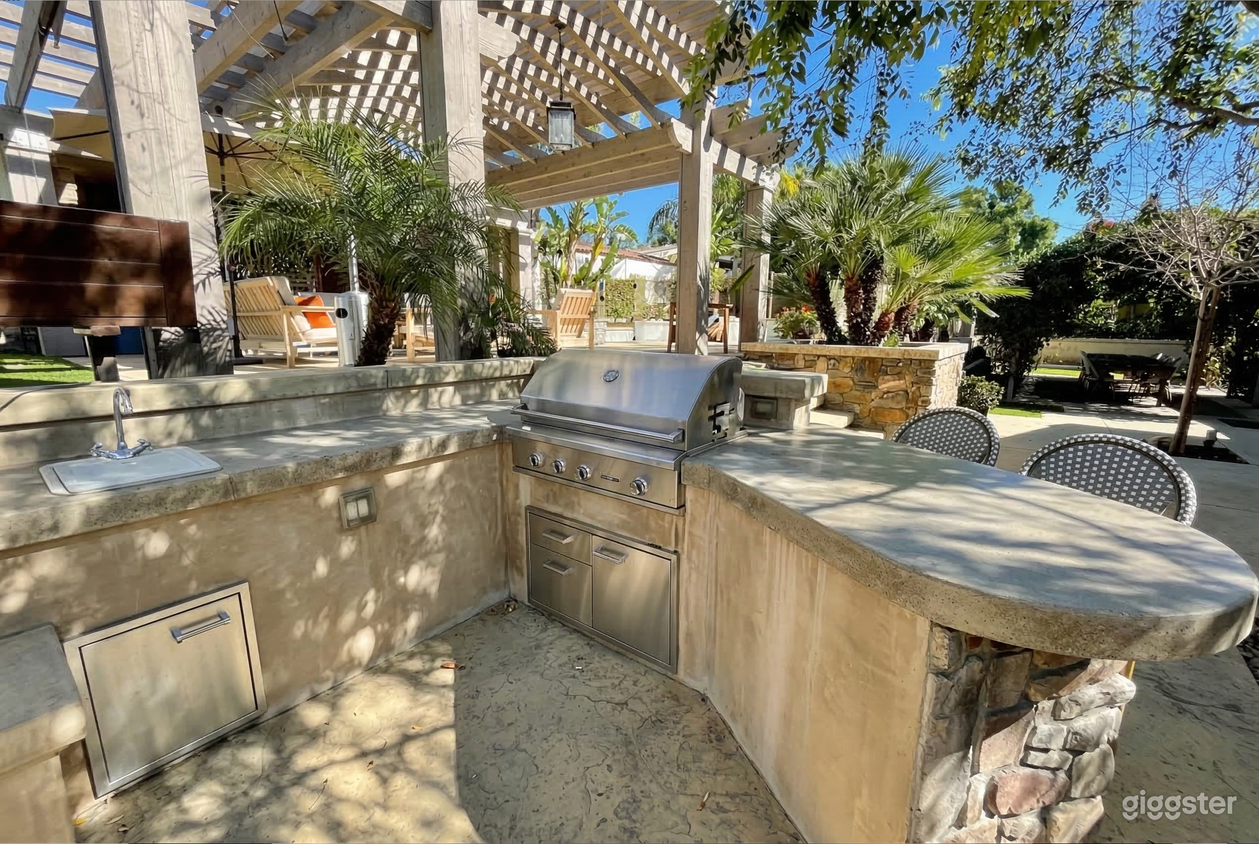 An barbecue area with stone countertops is the focal point of an outdoor kitchen with hedges and succulents.