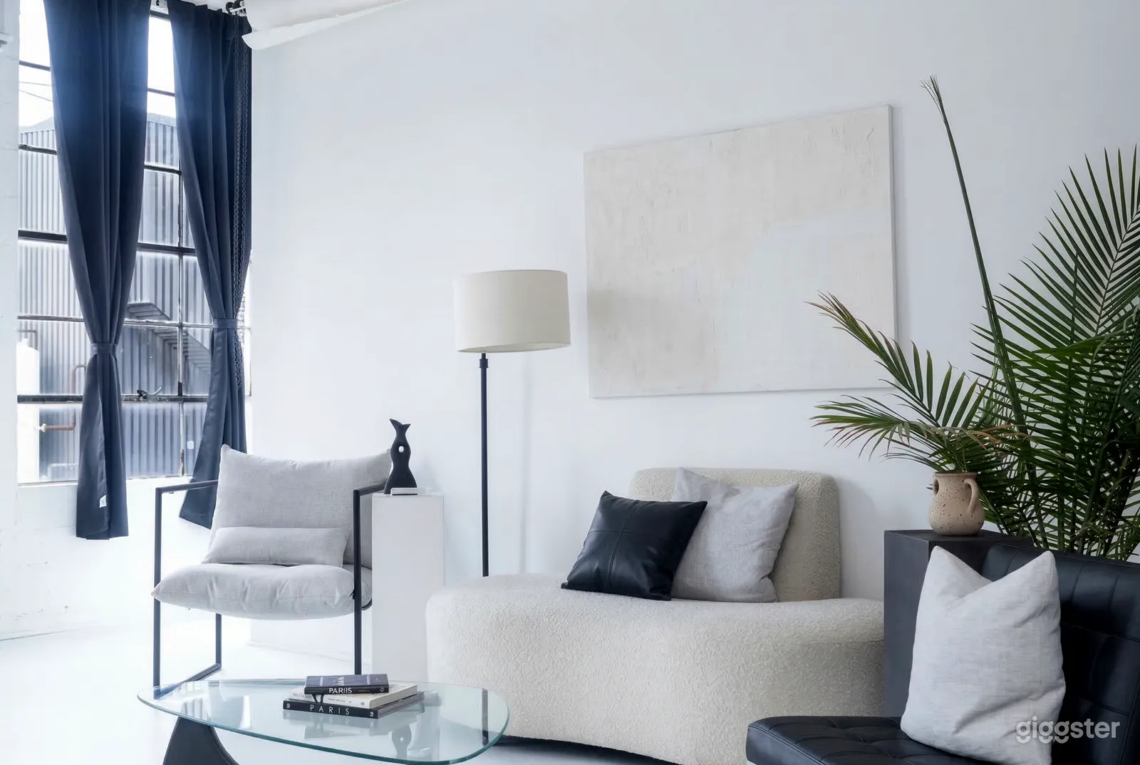 A modern room with black and white seating, a tall lamp, and branching out fern.