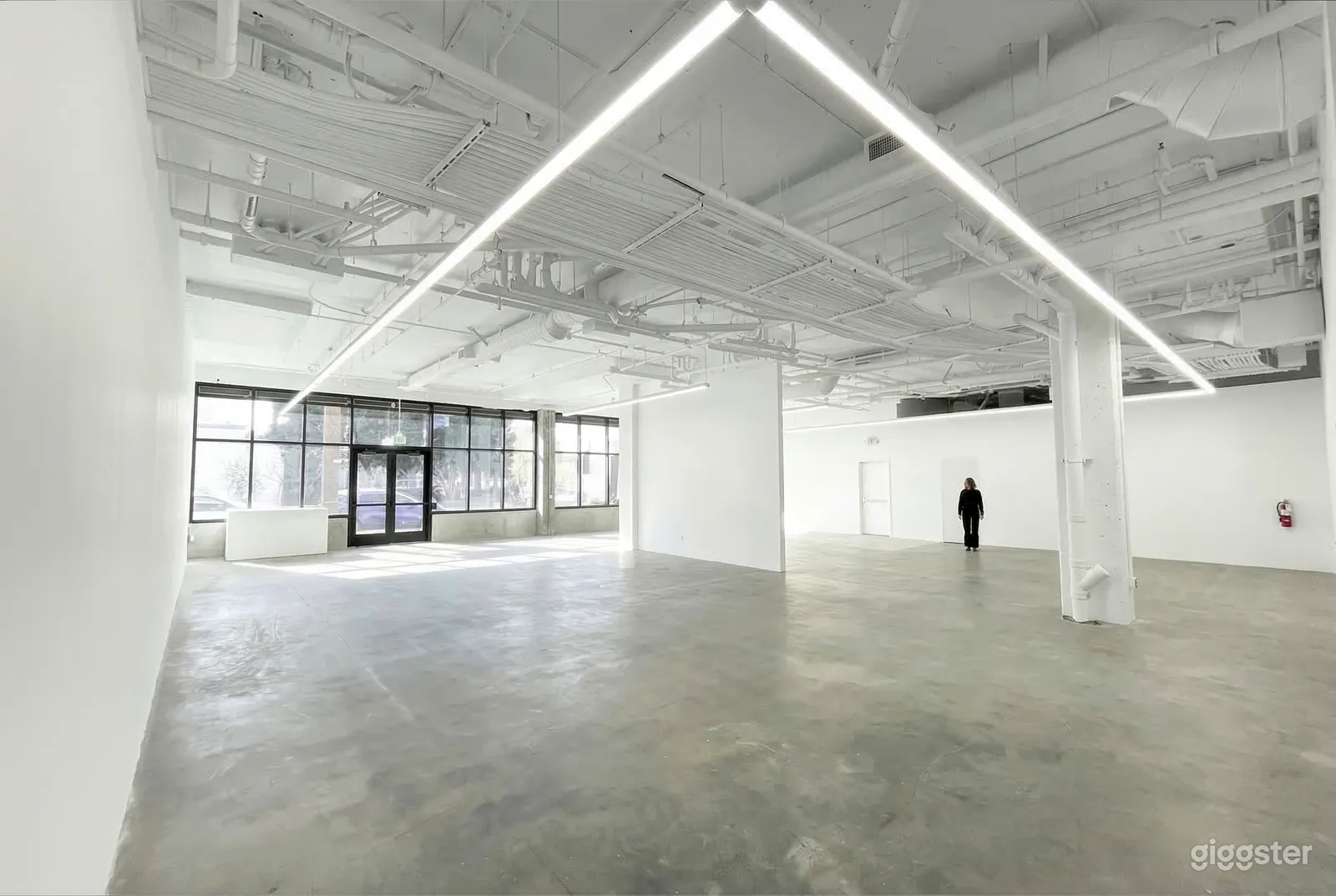 An empty white warehouse type space with one wall of windows and an industrial type ceiling painted white.