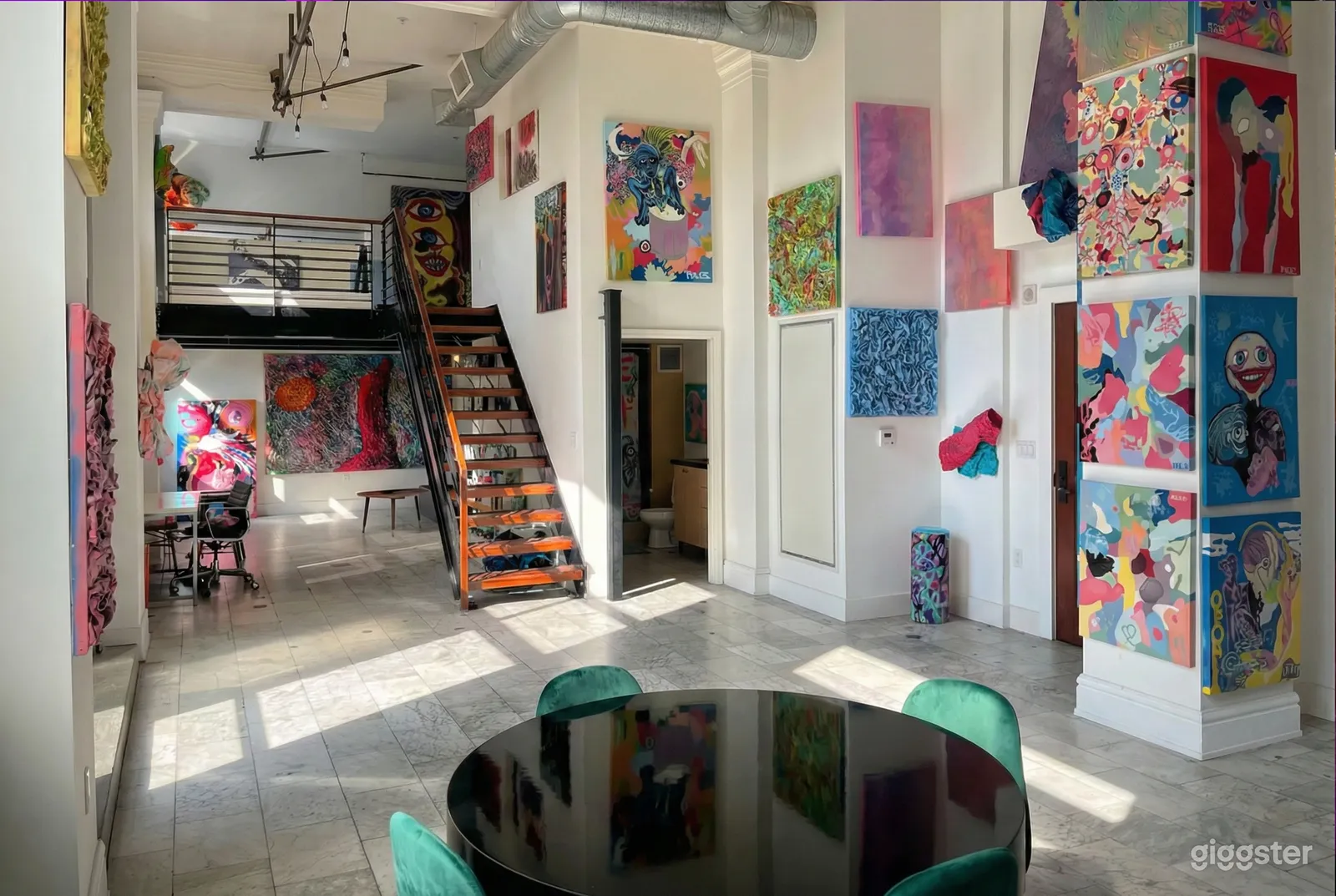 Bright room with multiple paintings on the wall and a central staircase.