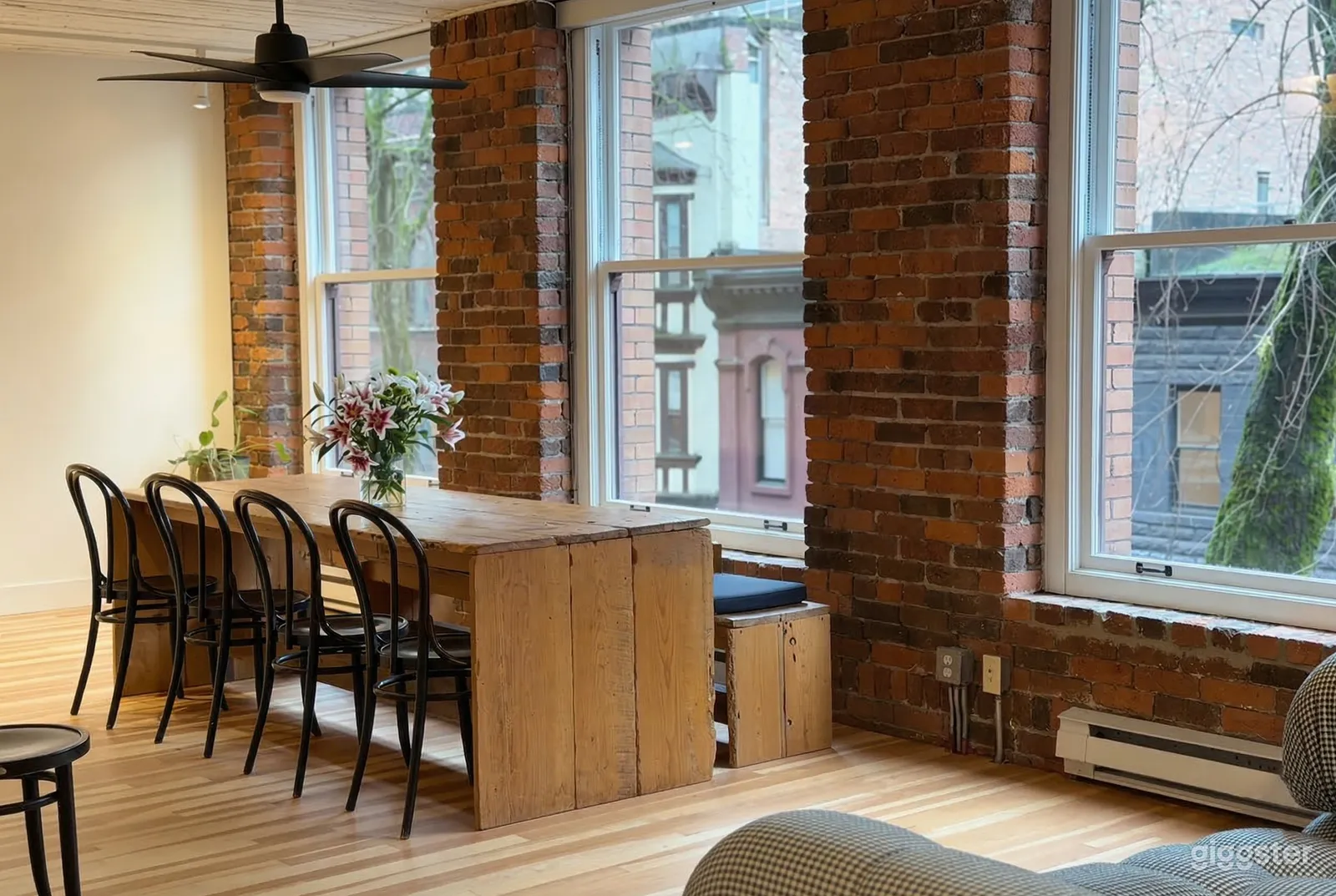 A rustic table with chairs and benches sits in front of an industrial type brick wall with windows.
