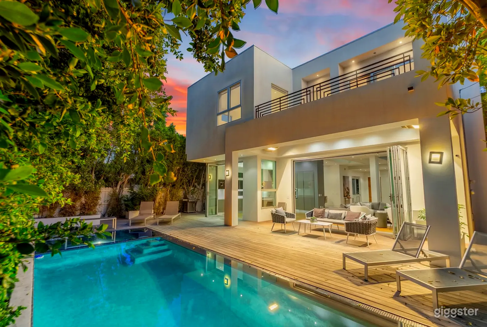 A white ultra modern home overlooks a pool and outdoor living room area.