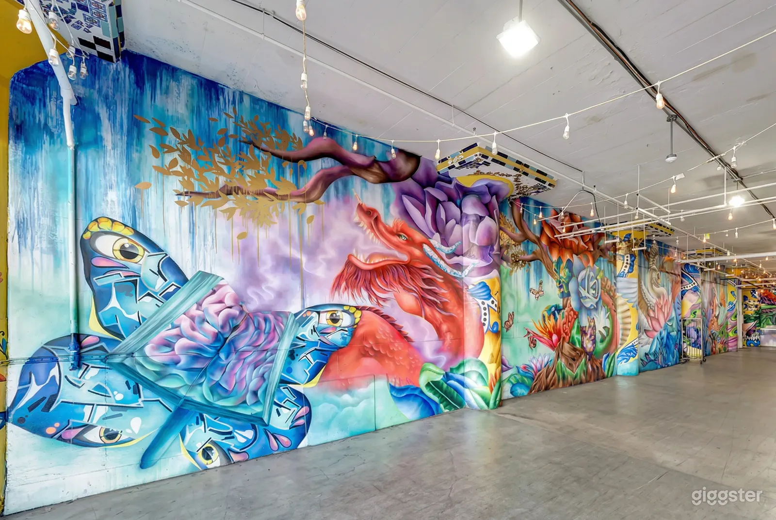 A studio wall is painted with a colorful mural and has rows of hanging lightbulbs overhead.