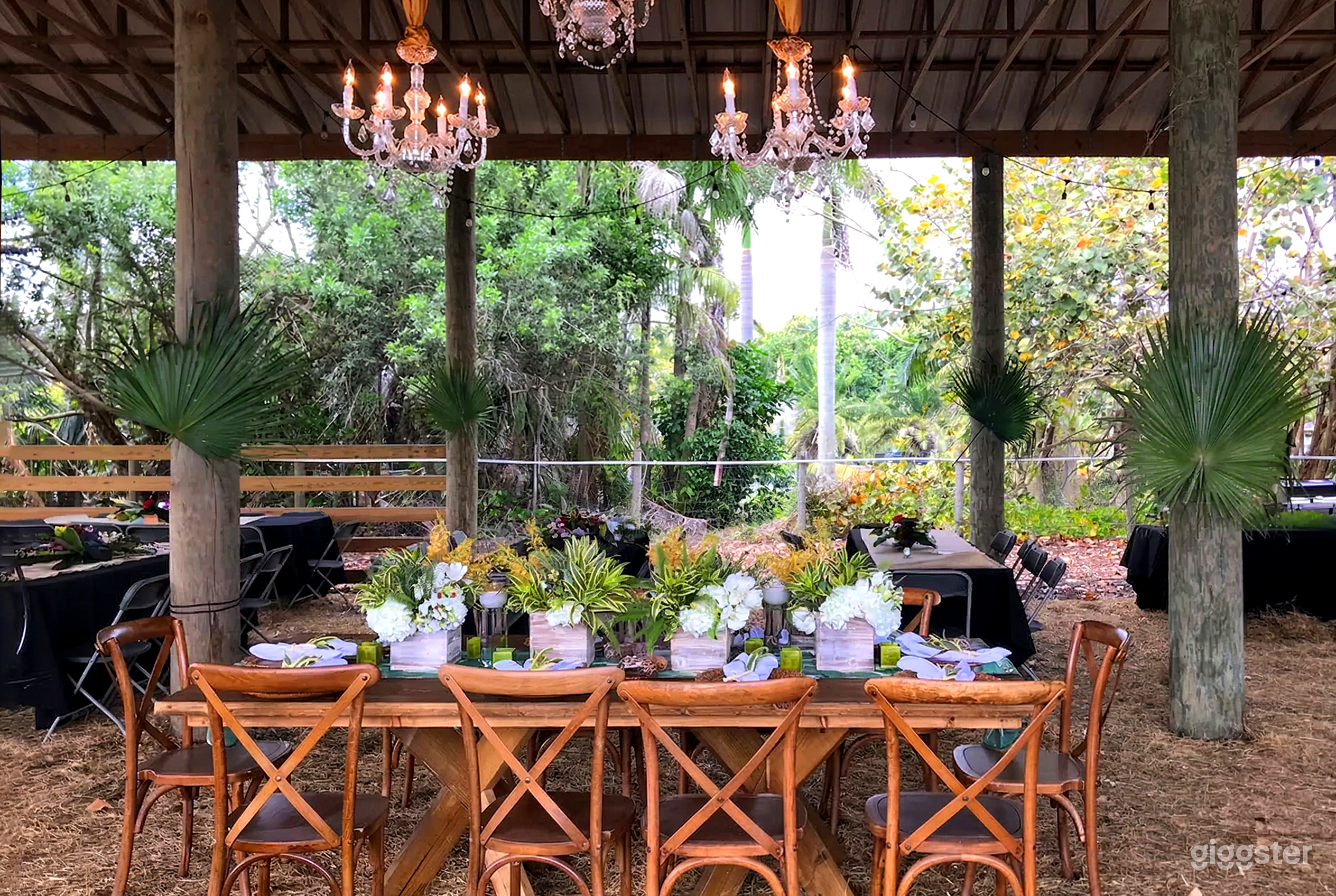 Three glass chandeliers hang over tables underneath a covered area surrounded by desert plants.