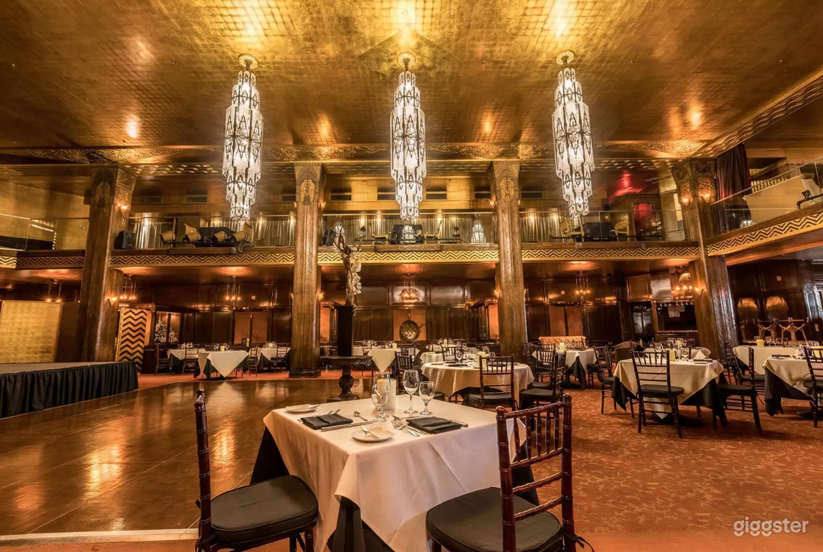 Expansive two level party room filled with tables and chairs, with three chandeliers as a focal point in the room.