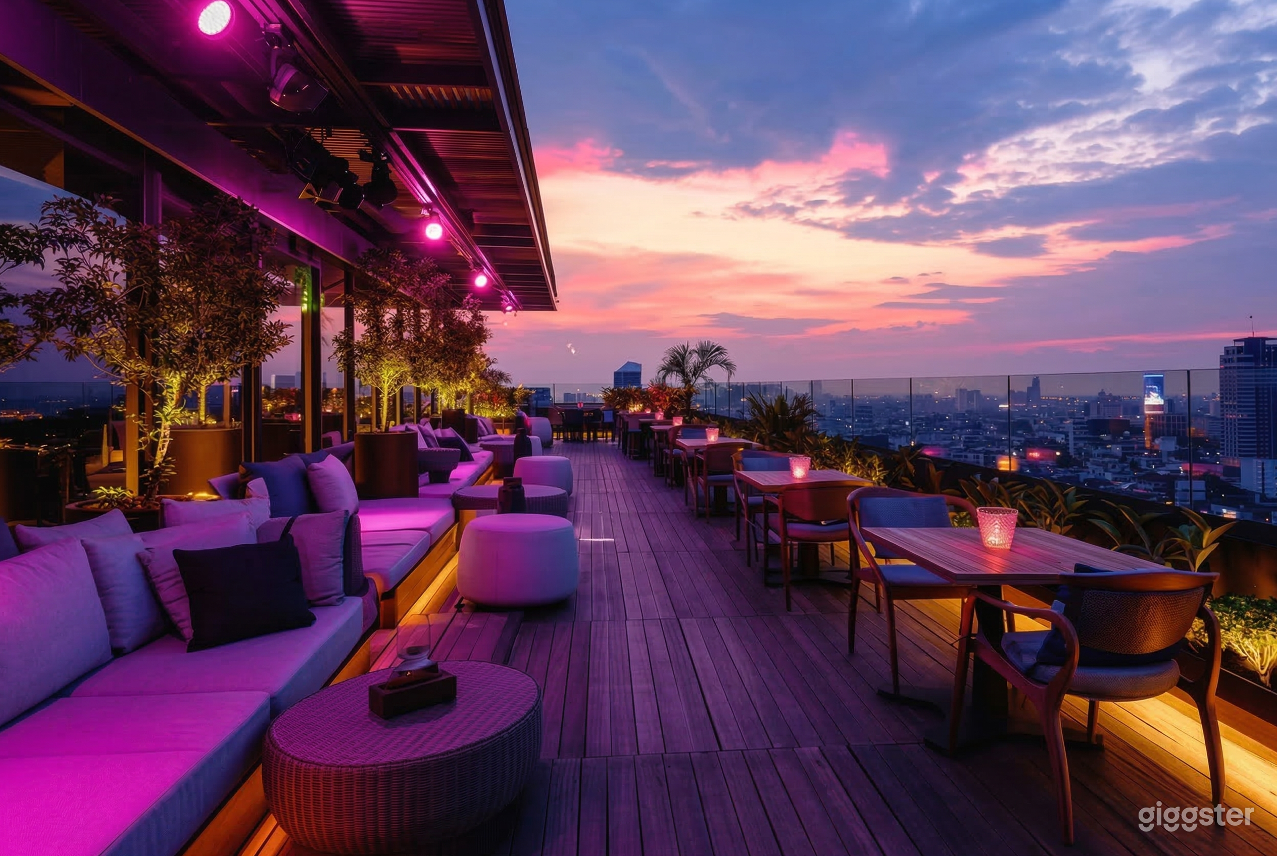 A large rooftop restaurant and lounge with tables, chairs, and comfortable couches is seen against a pink sunset.