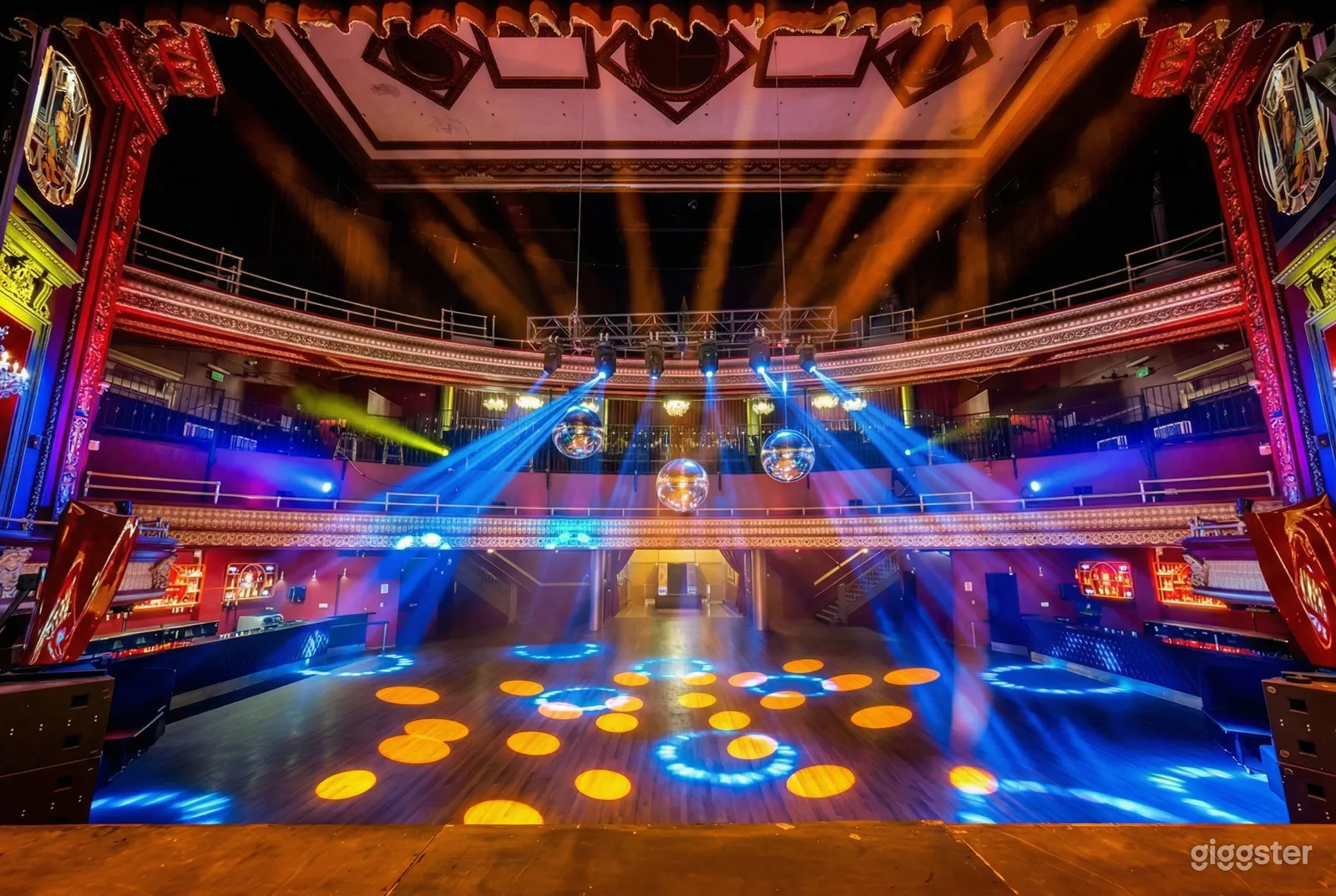 Blue strobe lights are pointed on a colorfully lit dance floor with disco balls overhead.