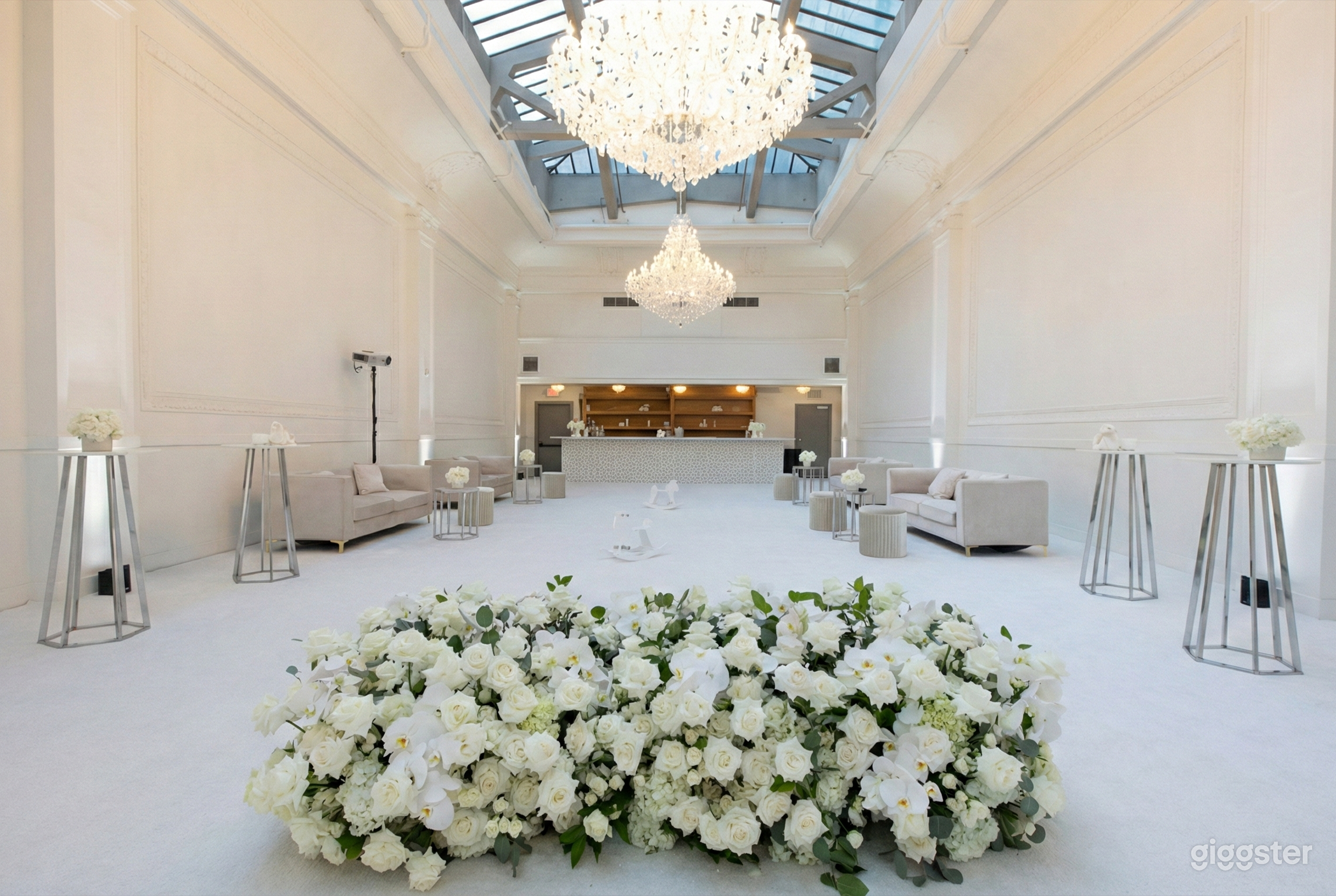 A modern room painted in white with a chandelier, couches, and wedding florals in the foreground.