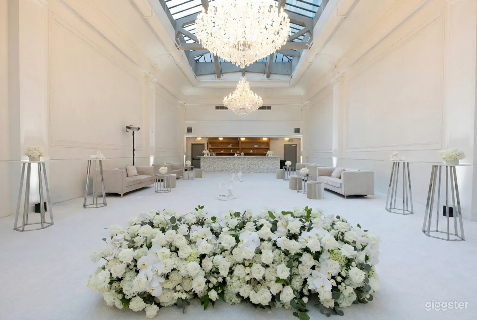 A modern room painted in white with a chandelier, couches, and wedding florals in the foreground.