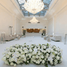 A modern room painted in white with a chandelier, couches, and wedding florals in the foreground.