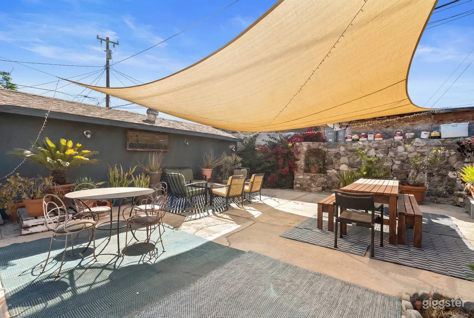 A breezy canopy covers a stone terrace with various styled tables and chairs in front of a rock and cement wall.