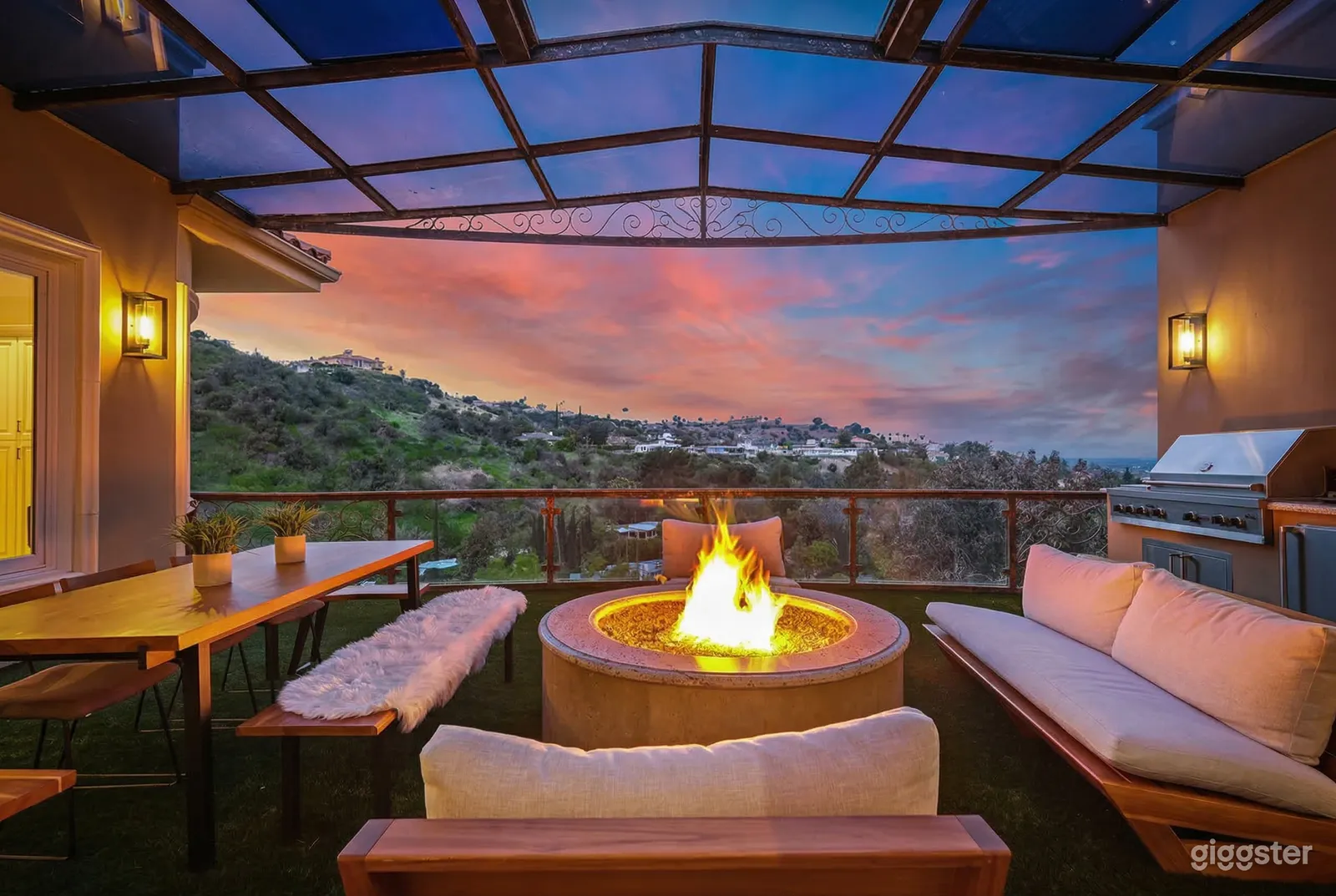 Comfortable benches face a round fireplace on a covered patio with one side open to the sky.