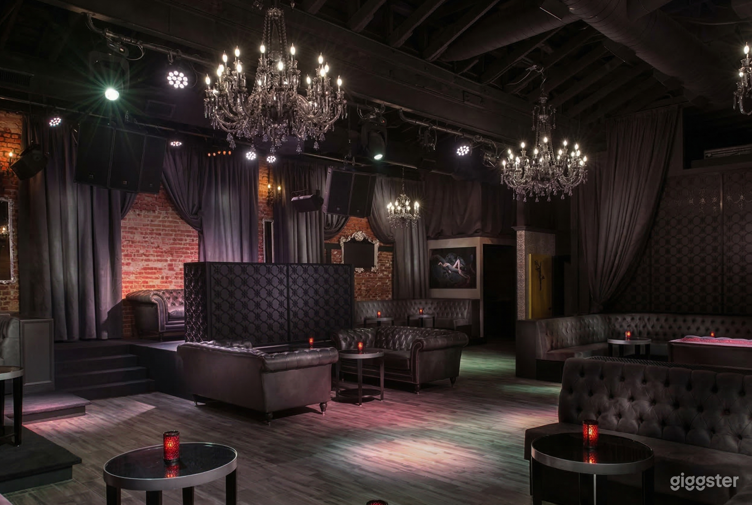 A room is decorated in black leather furniture and curtains, with statement chandeliers and lighting overhead.
