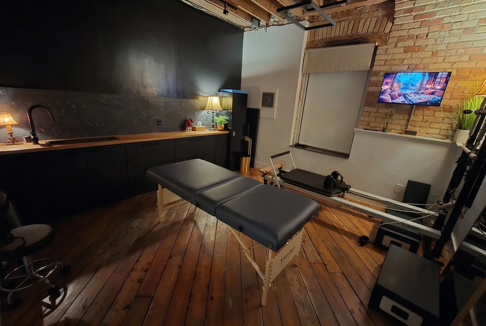 A cushioned therapy table and a Pilates reformer machine sit in front of a long countertop with a sink.