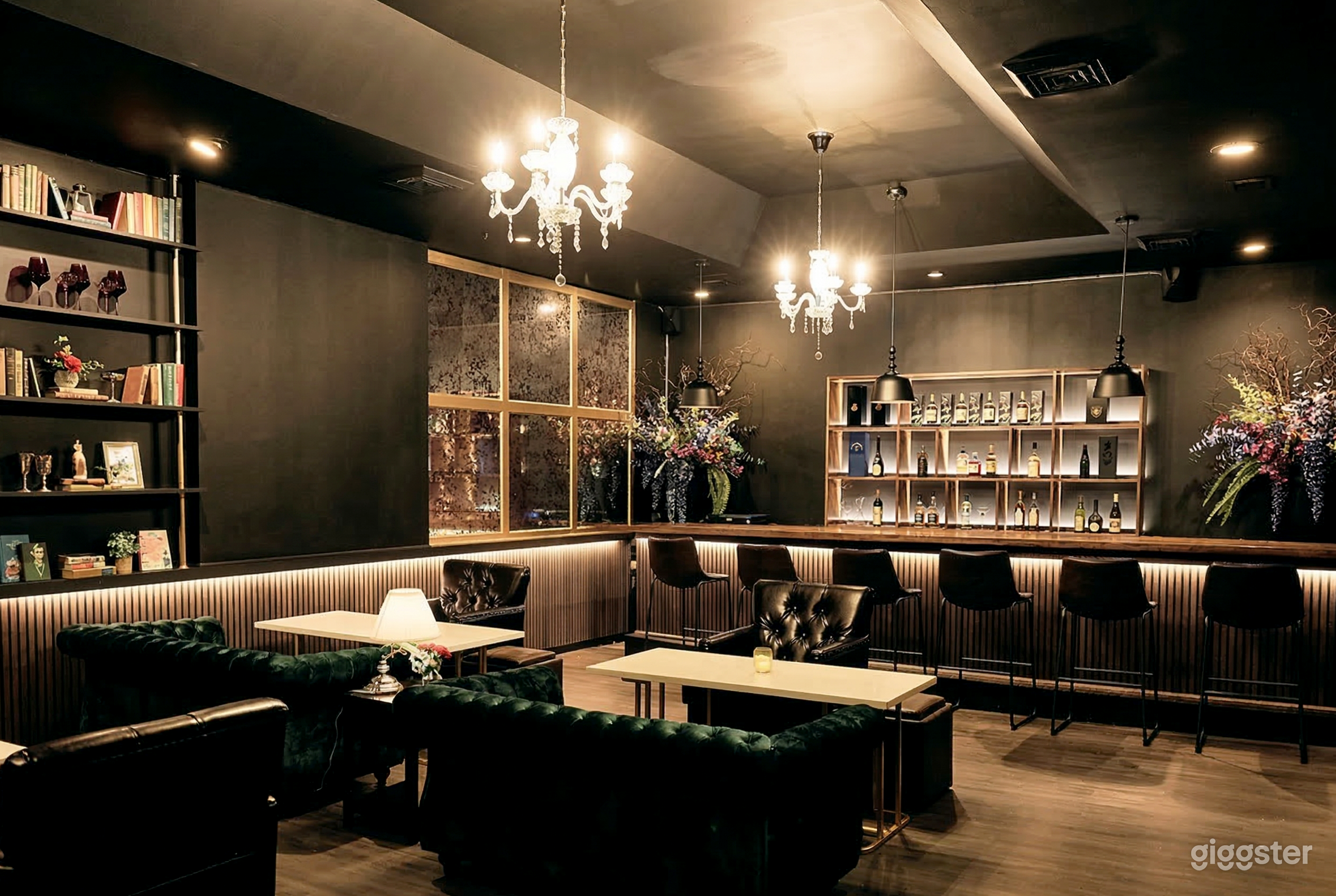 Tall seating lines an elaborate  and well-lit bar, and table with green velvet benches are behind them.