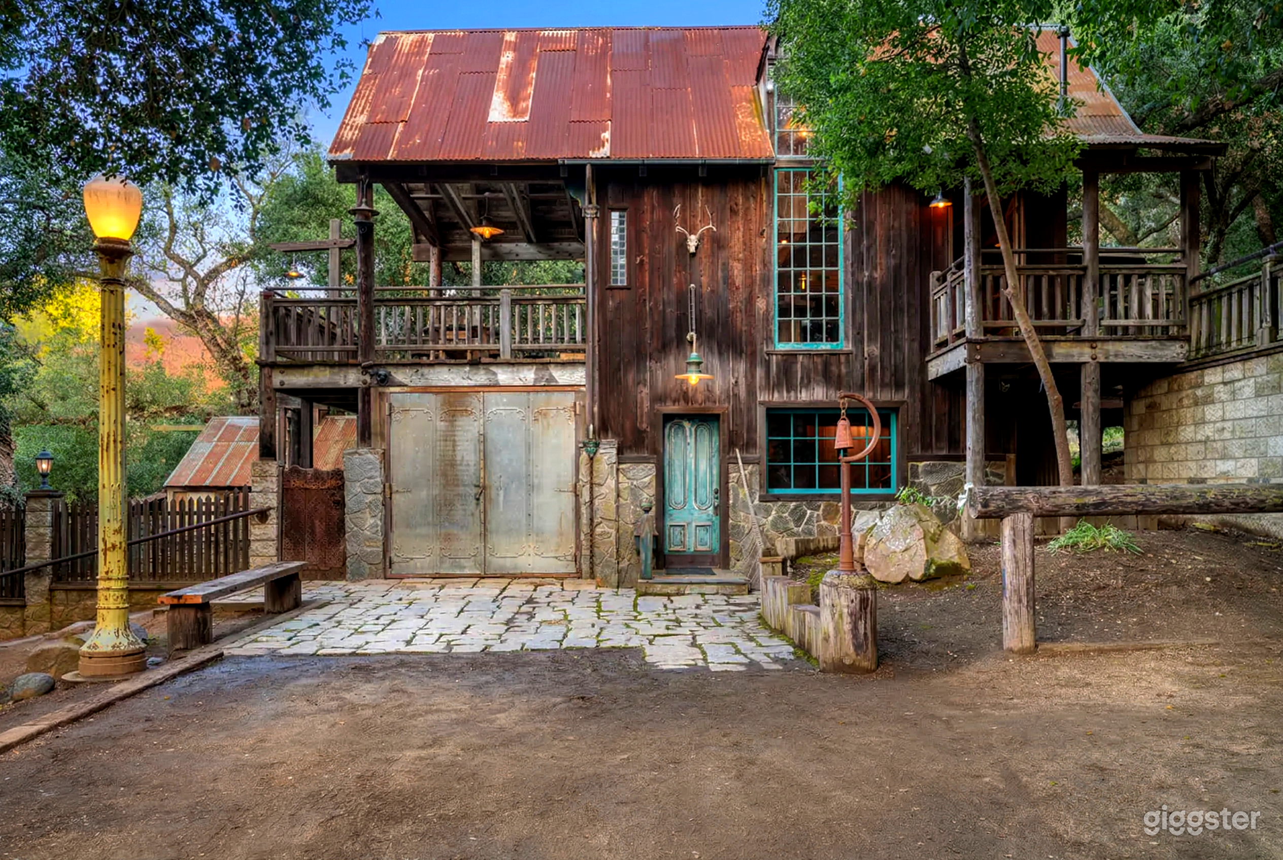 A rustic style home has a turquoise lined windows and door with two outdoor seating areas. 