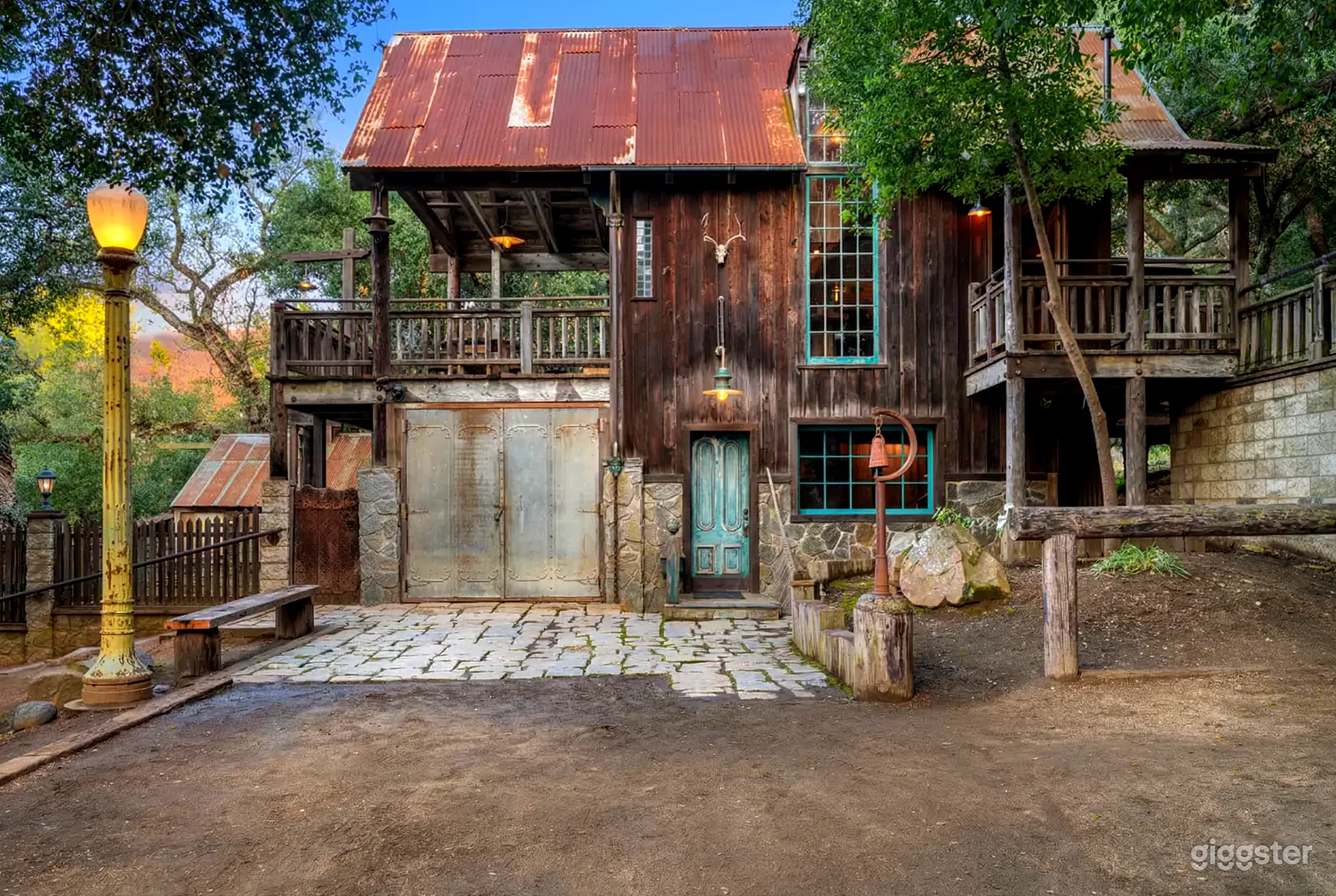 A rustic style home has a turquoise lined windows and door with two outdoor seating areas. 