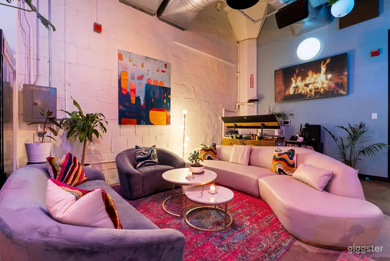 Curvy pink and purple couches face each other in an industrial type room with large pictures on the wall.