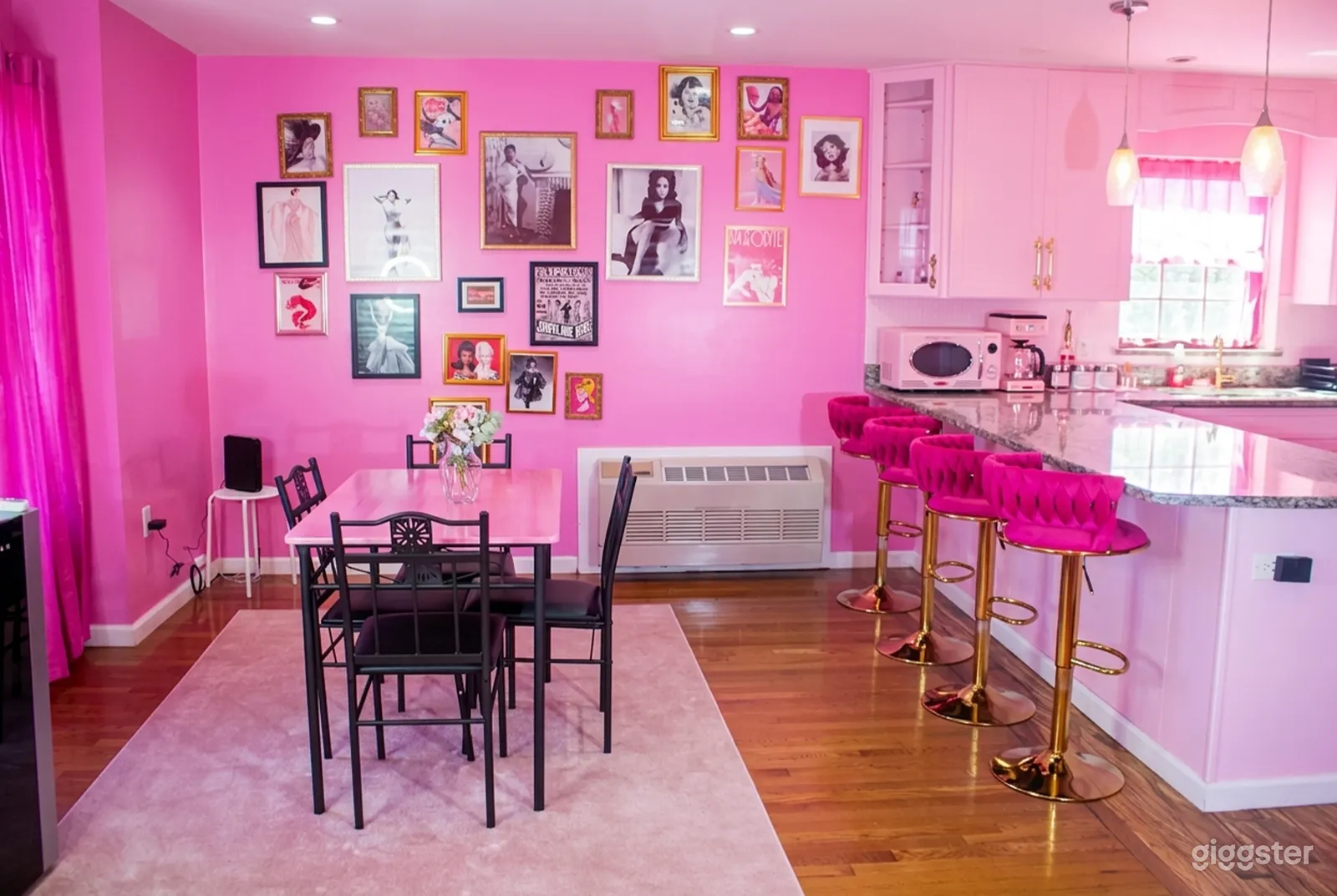 A dining room and kitchen is decorated entirely in pink, with walls, cabinets and cushioned stools all in shades of pink.
