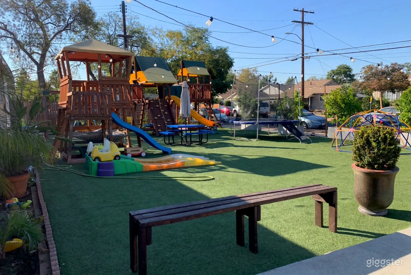 A children's park has multiple slides, a climbing structure and a trampoline all situated on artificial turf.