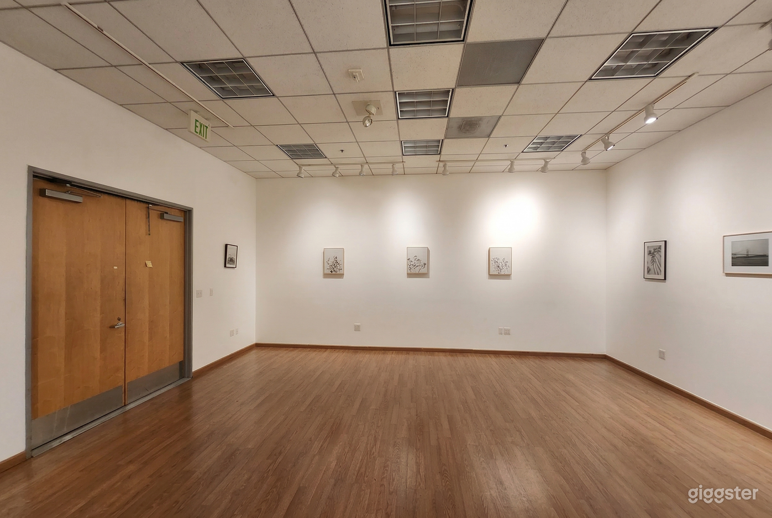 A wide open gallery space with minimal small paintings and photos on a white wall.