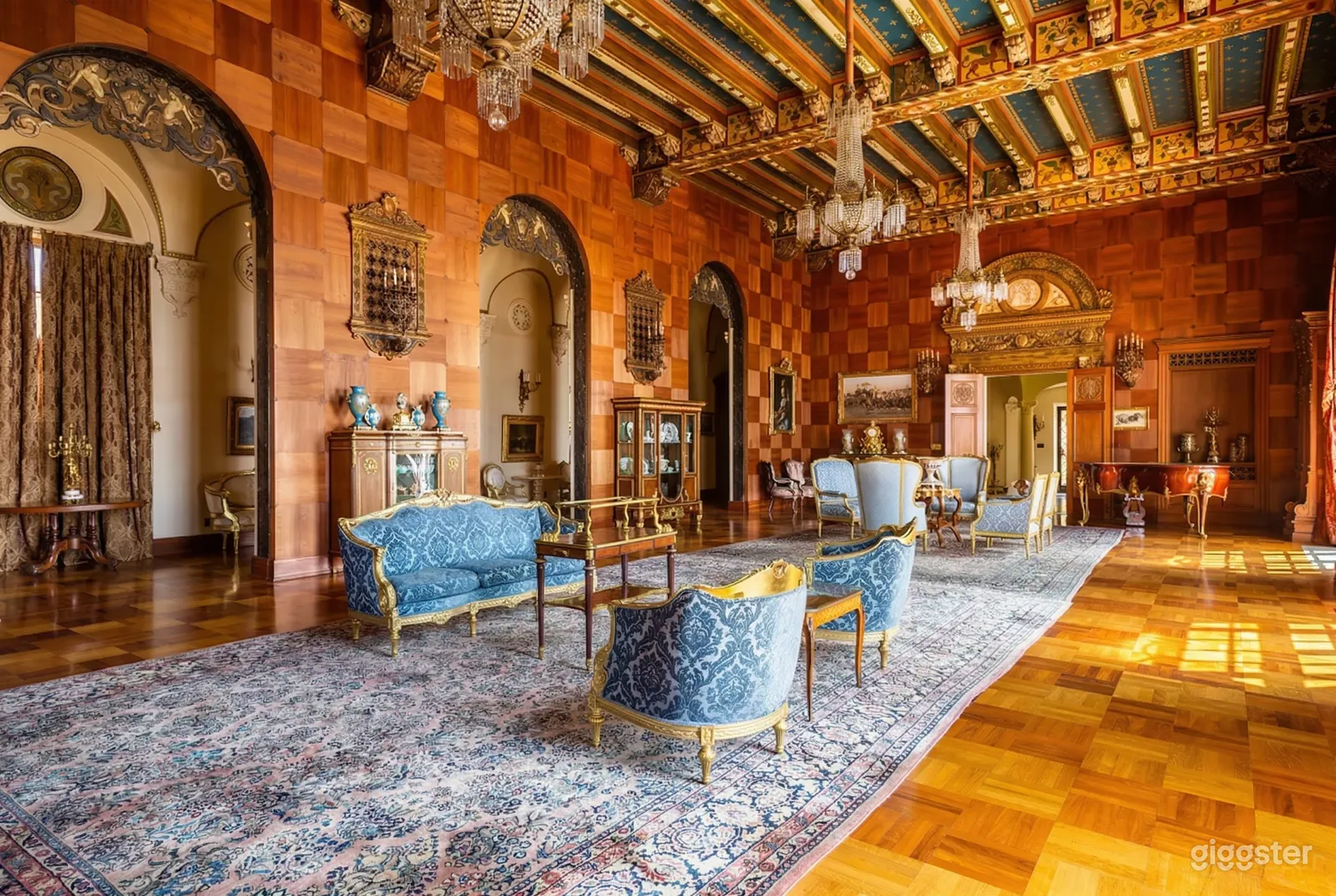 A Victorianesque room has two shades of blue couches and chairs with curio cabinets along a wall with wood detailing.