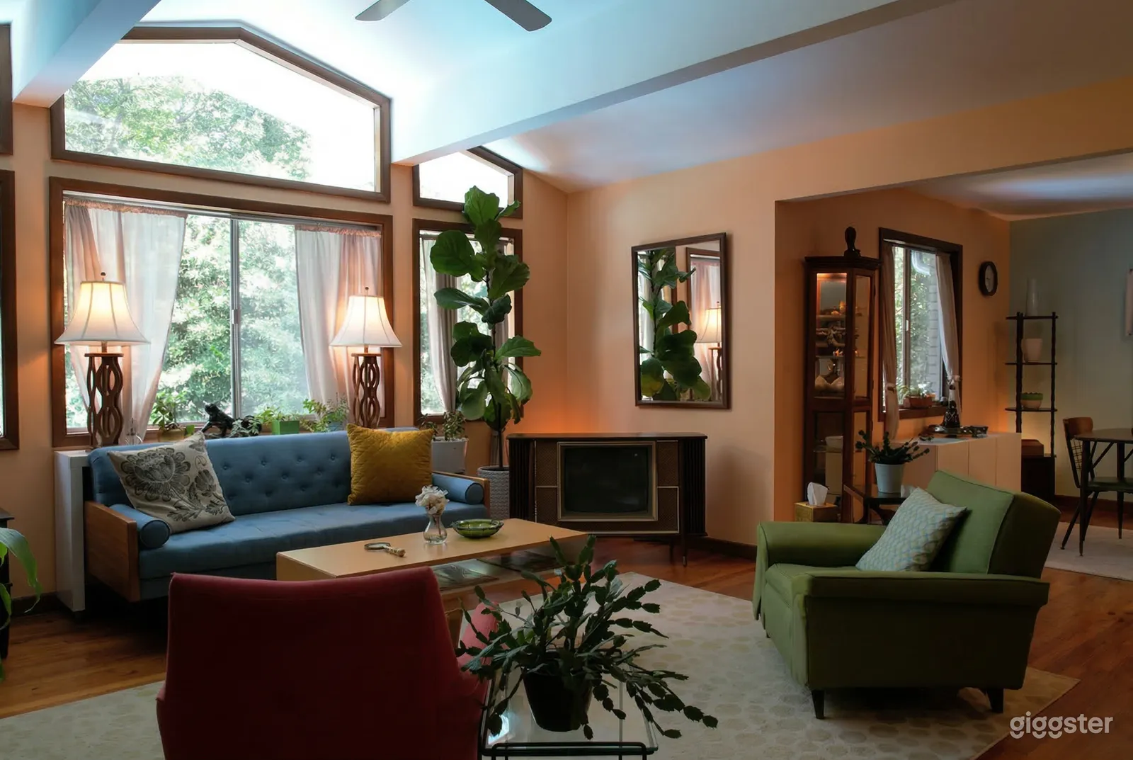 A mid century modern room is decorated with colorful couches, vintage lamps and pillows, and tall plants.