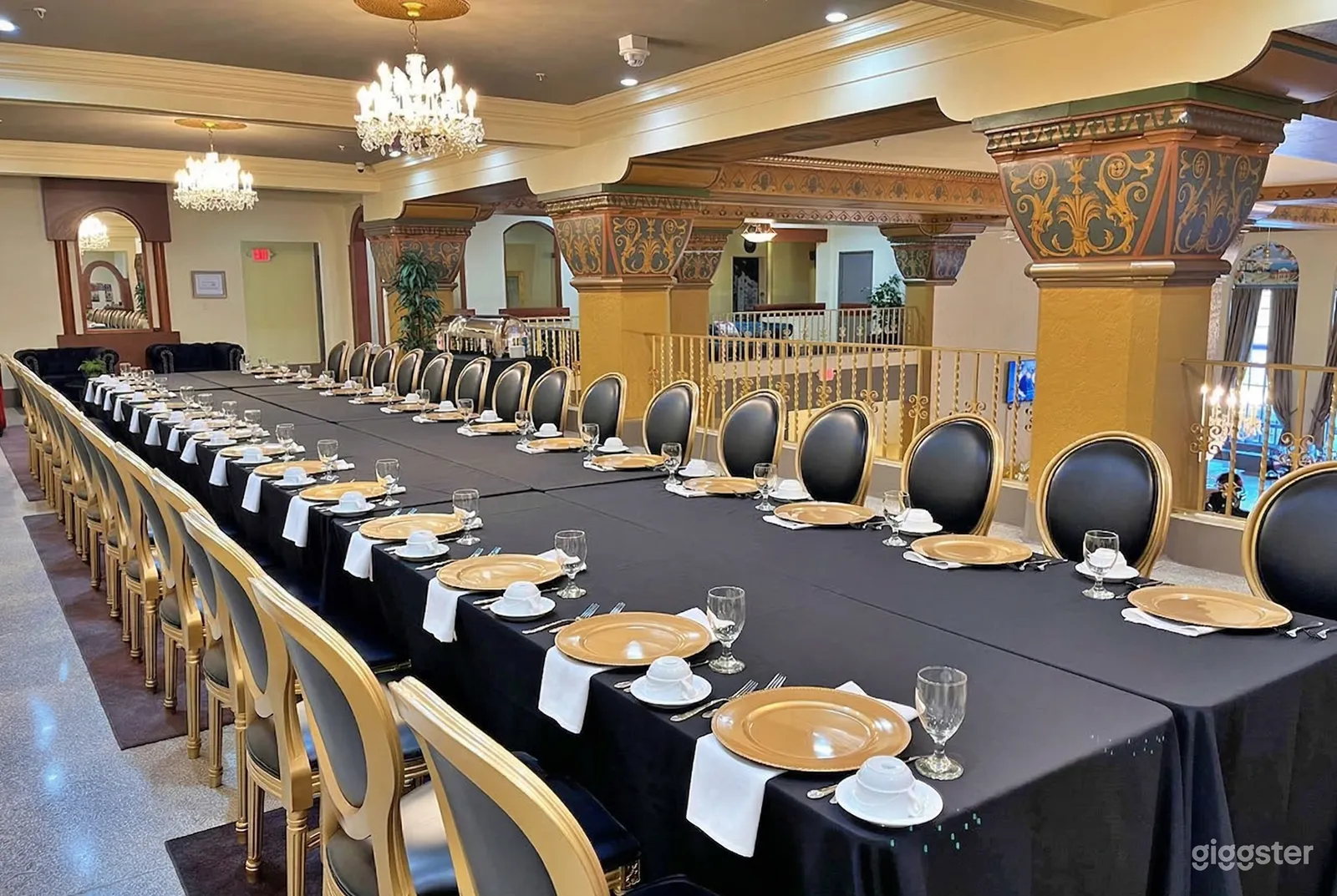 A long dining table is set in black and gold with large ornate columns as the restaurant backdrop.