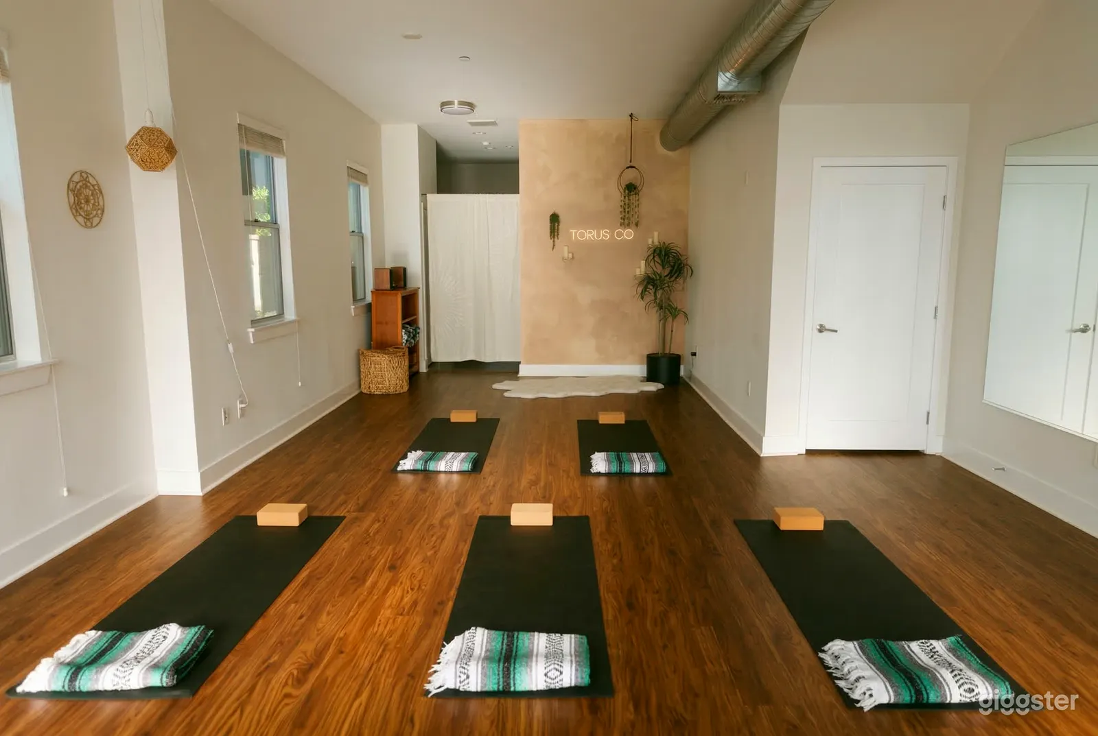 A studio with brown wood floors has 5 yoga mats, blankets, and blocks set up for a session.