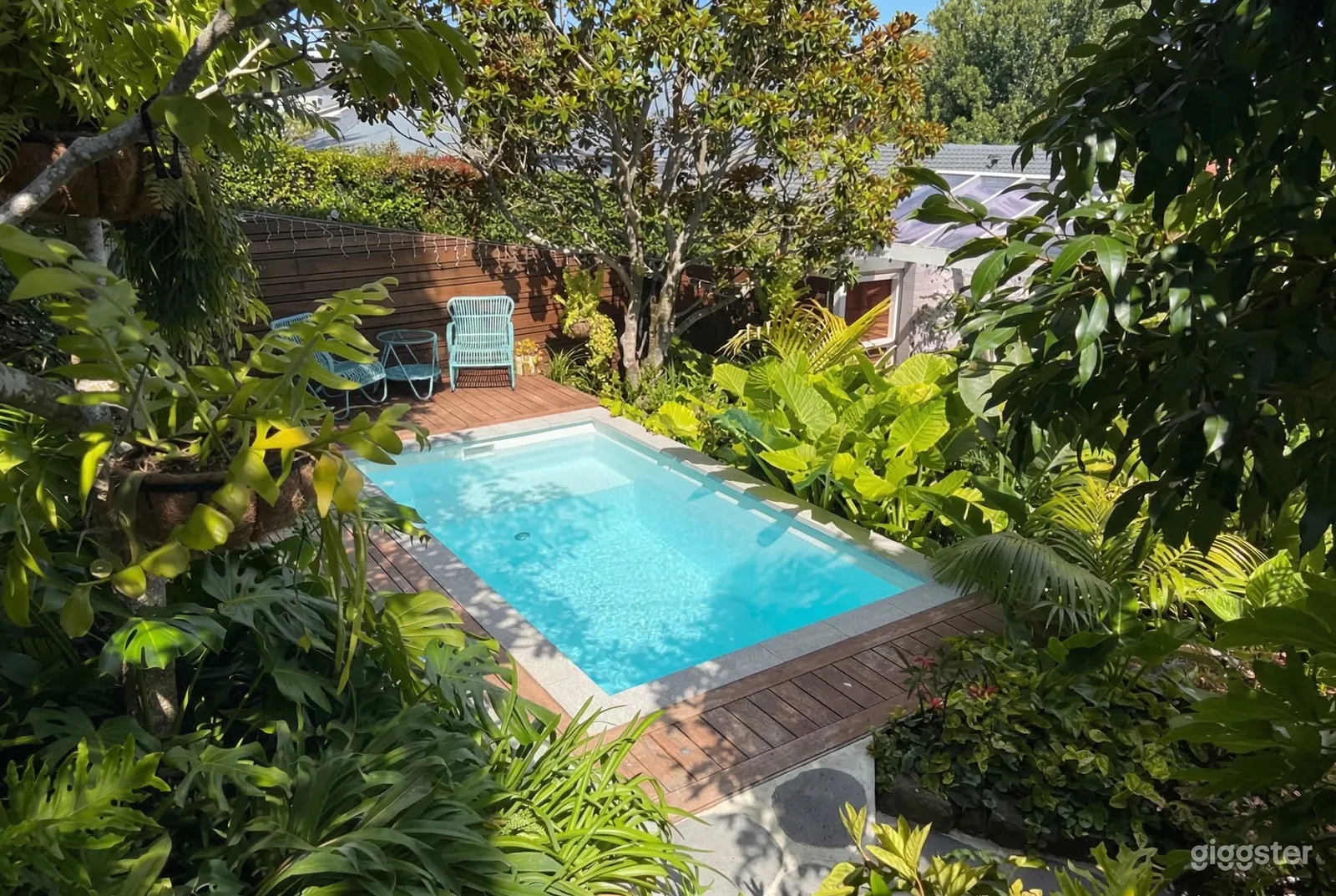 A swimming pool is surrounded by lush tropical gardens and wood decking.