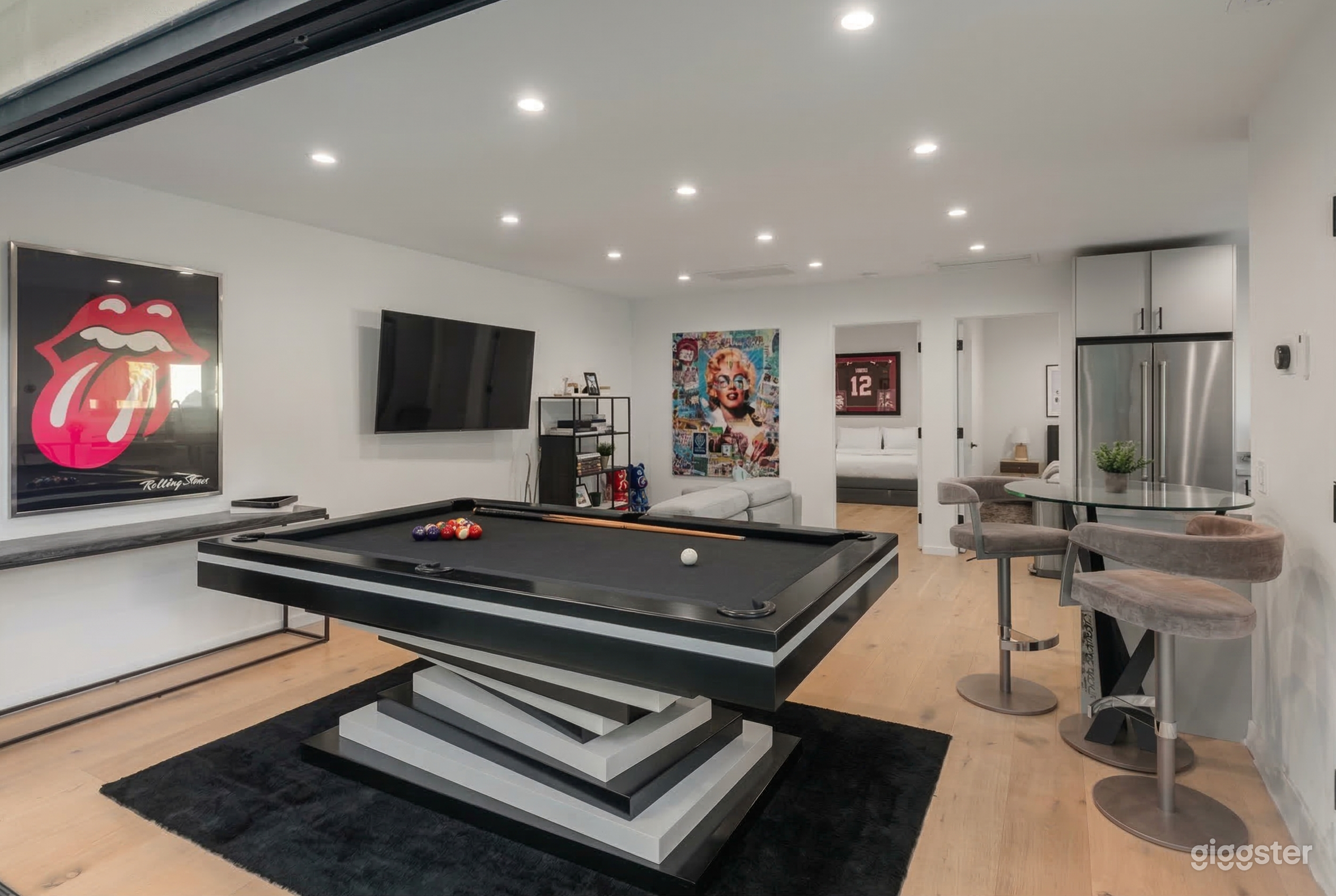 A pool table is central in a white-painted room with posters and a large TV on the wall.