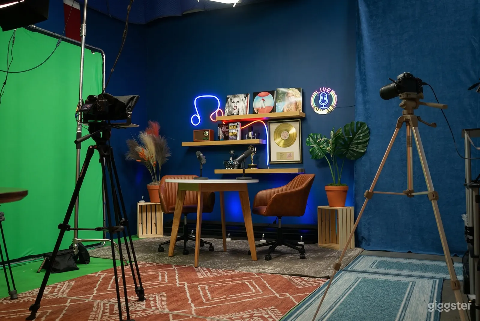 A two-chair podcast set up sits in front of a blue curtained wall and a green screen.