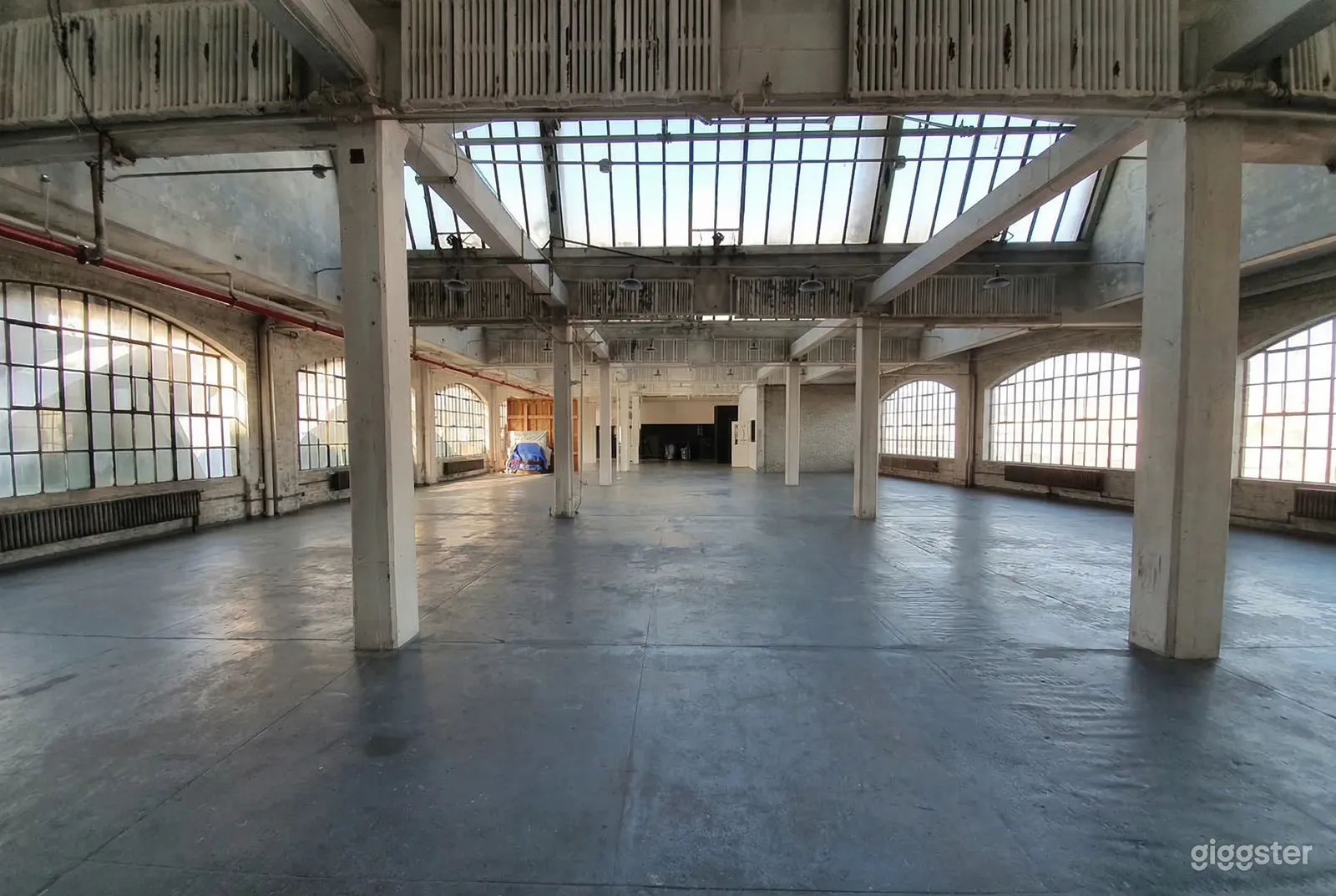 A massive industrial style room has cement flooring with large bulky columns and big grated windows.