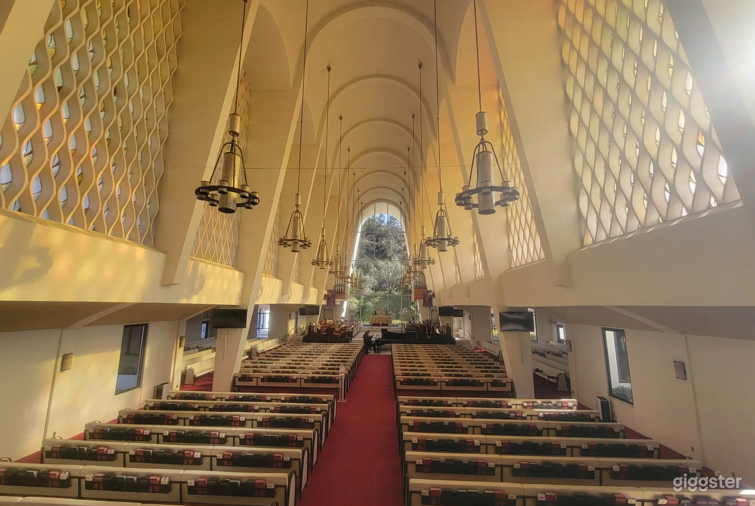 A curved detailed ceiling with several chandeliers is the focal point of a pew lined chapel with windows at the end.
