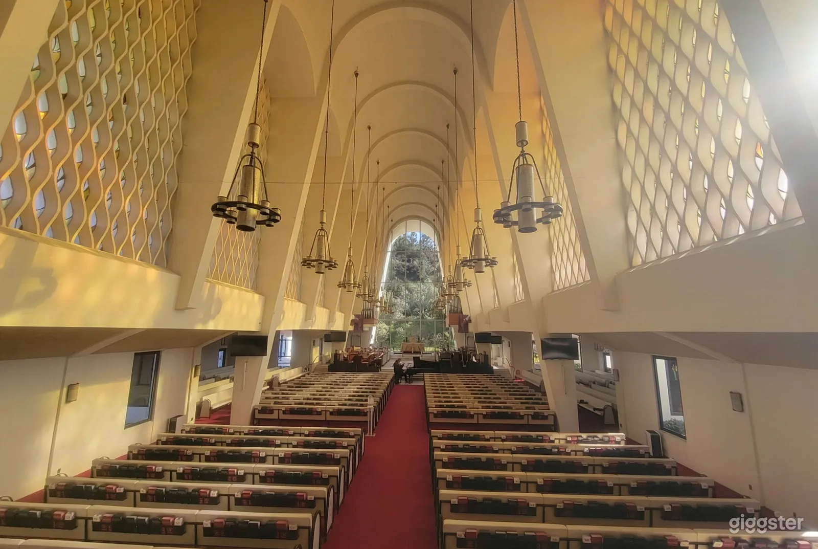 A curved detailed ceiling with several chandeliers is the focal point of a pew lined chapel with windows at the end.