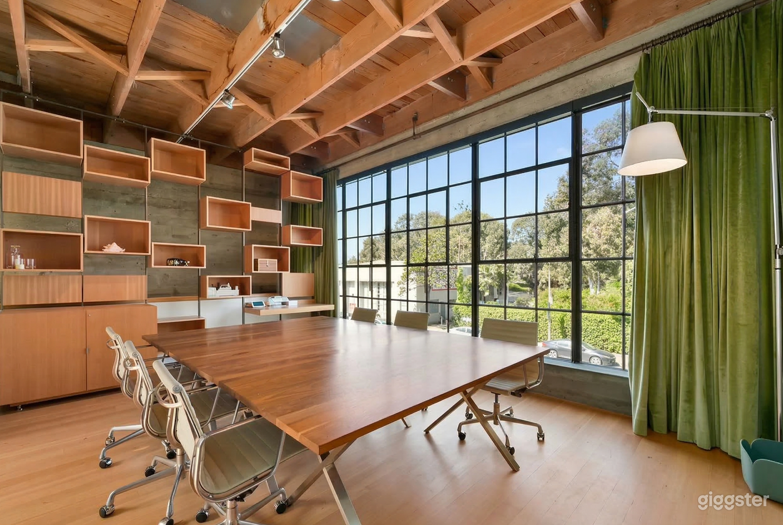 A modern conference room with a walled window has modular shelving and a large wooden conference table and chairs.