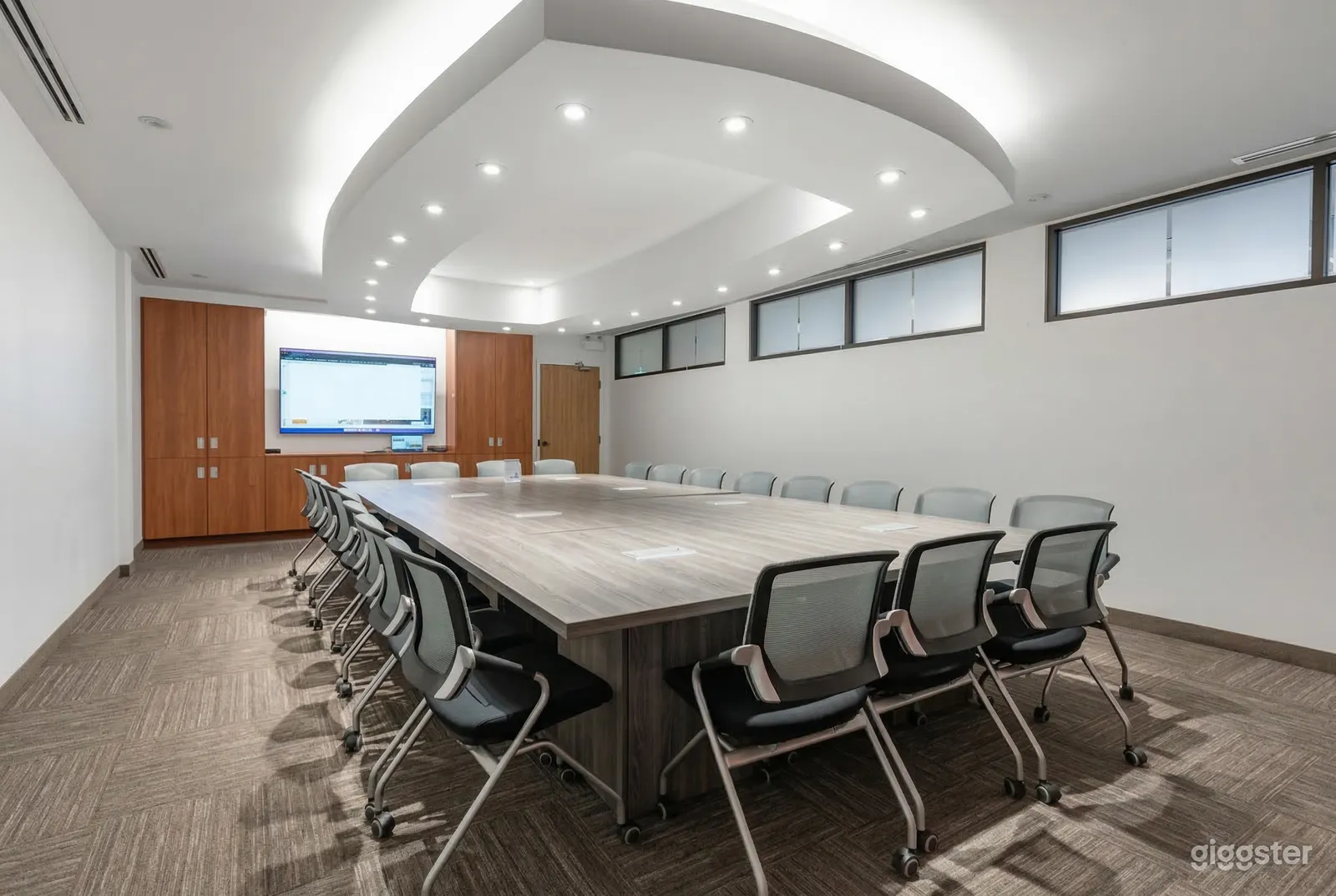 An extra large grey table and chairs fills a modern office and the room has a tech screen on one wall.