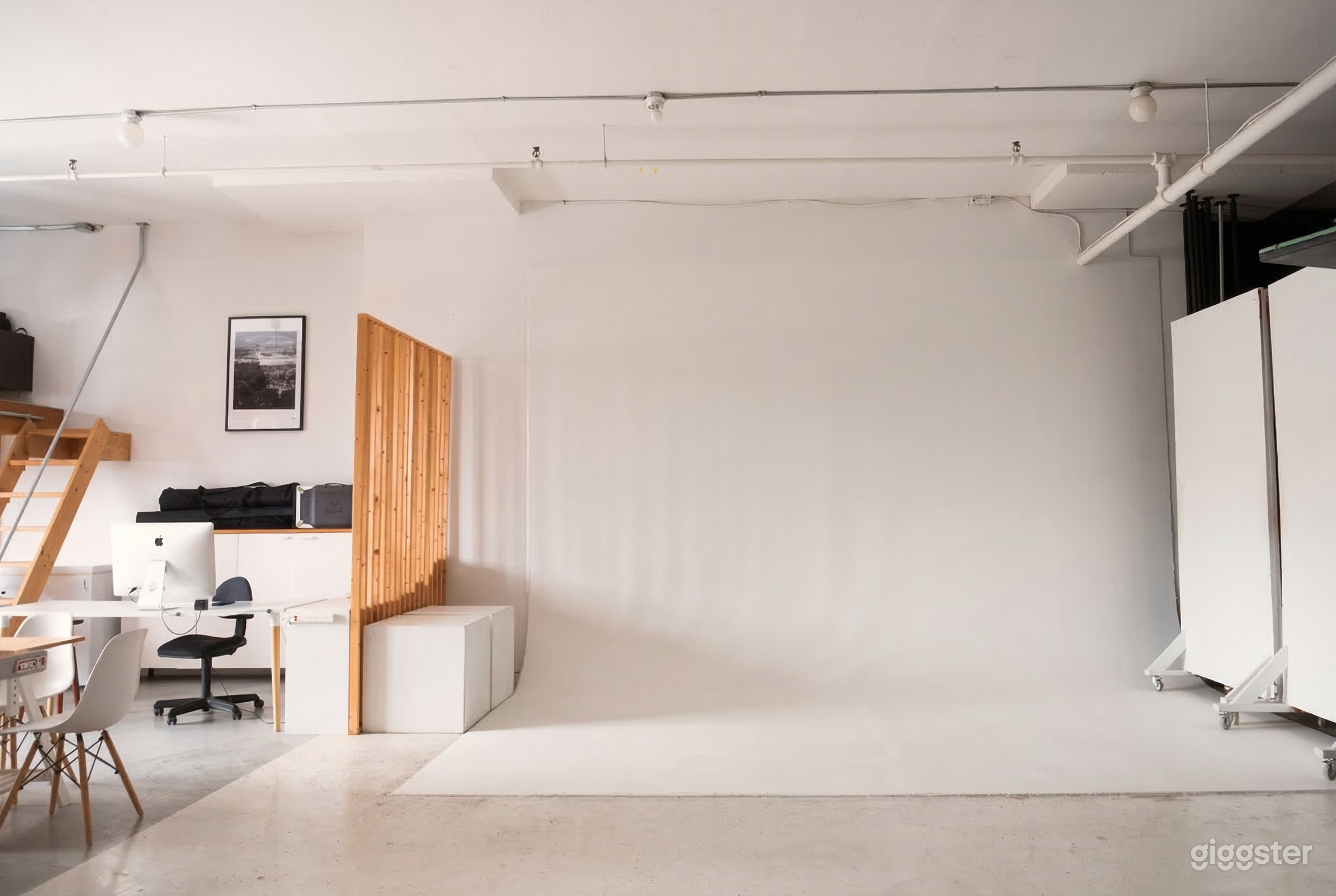 A white screen is central to a photo shoot studio, with a small office space off to the side.