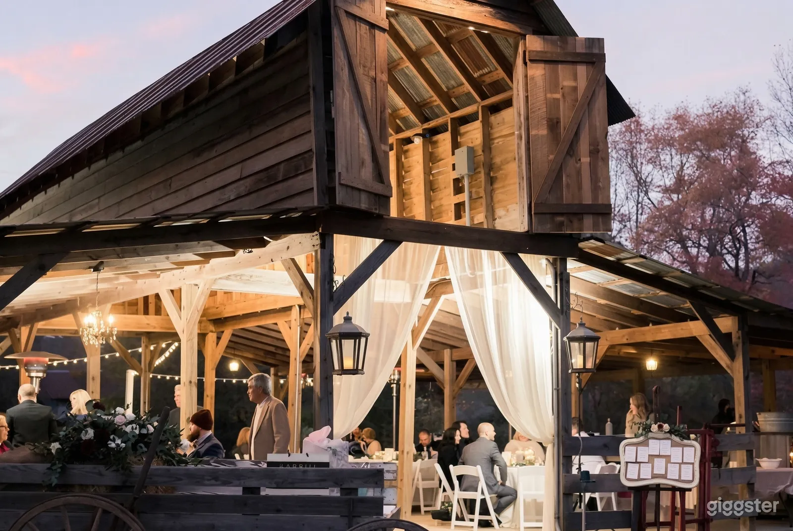 People sit inside a well-lit barn decorated with lighting and sheer curtains at the entrance.