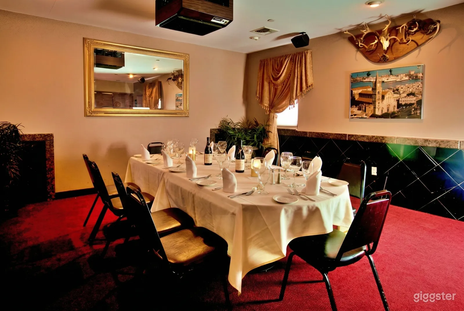 A dining room holds an oblong table decorated with a white tablecloth, napkins and wine glasses.