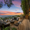 Couches chairs and stools overlook a city view on a wood rooftop patio with trees giving privacy on the side.