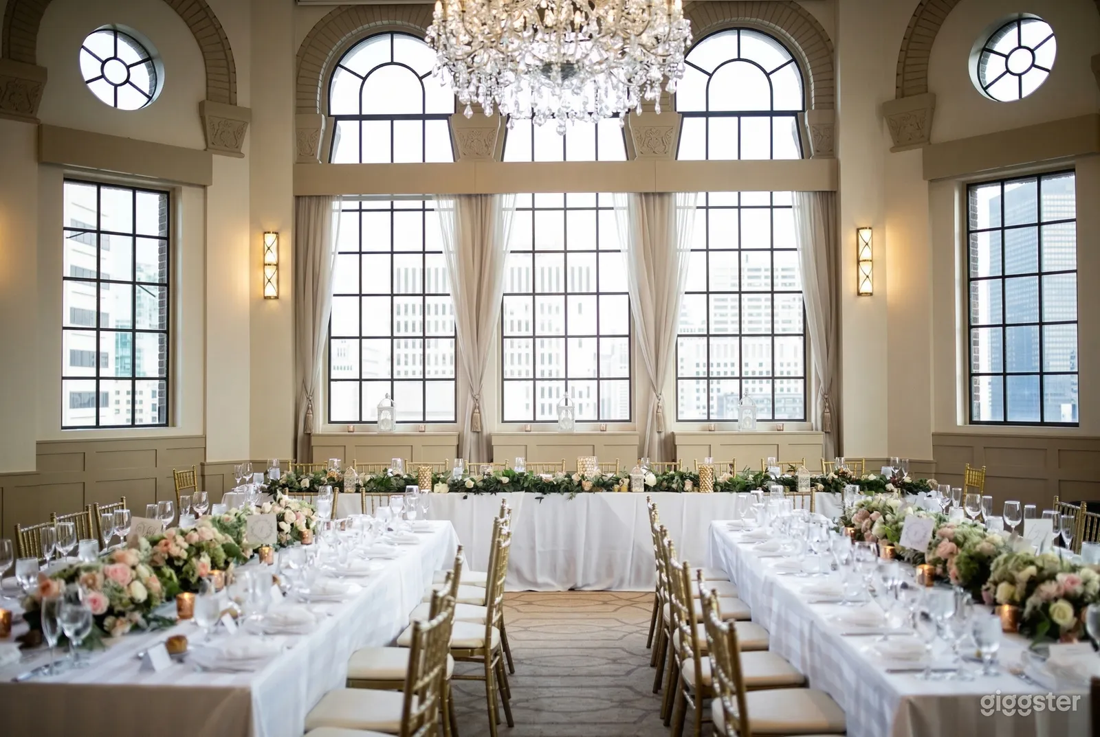 A hotel event room is filled with banquet tables and chairs decorated in floral centerpieces, with a paned, curved window at the front of the room.