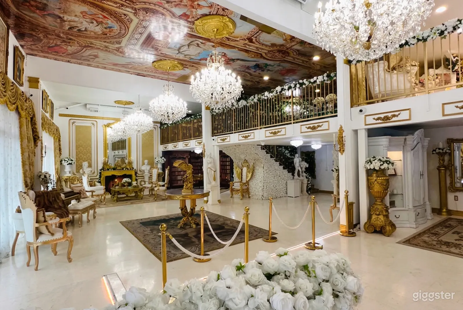 An ornately decorated ballroom venue with statues, carved bust figures, gold urns and tables, and five extravagant chandeliers.