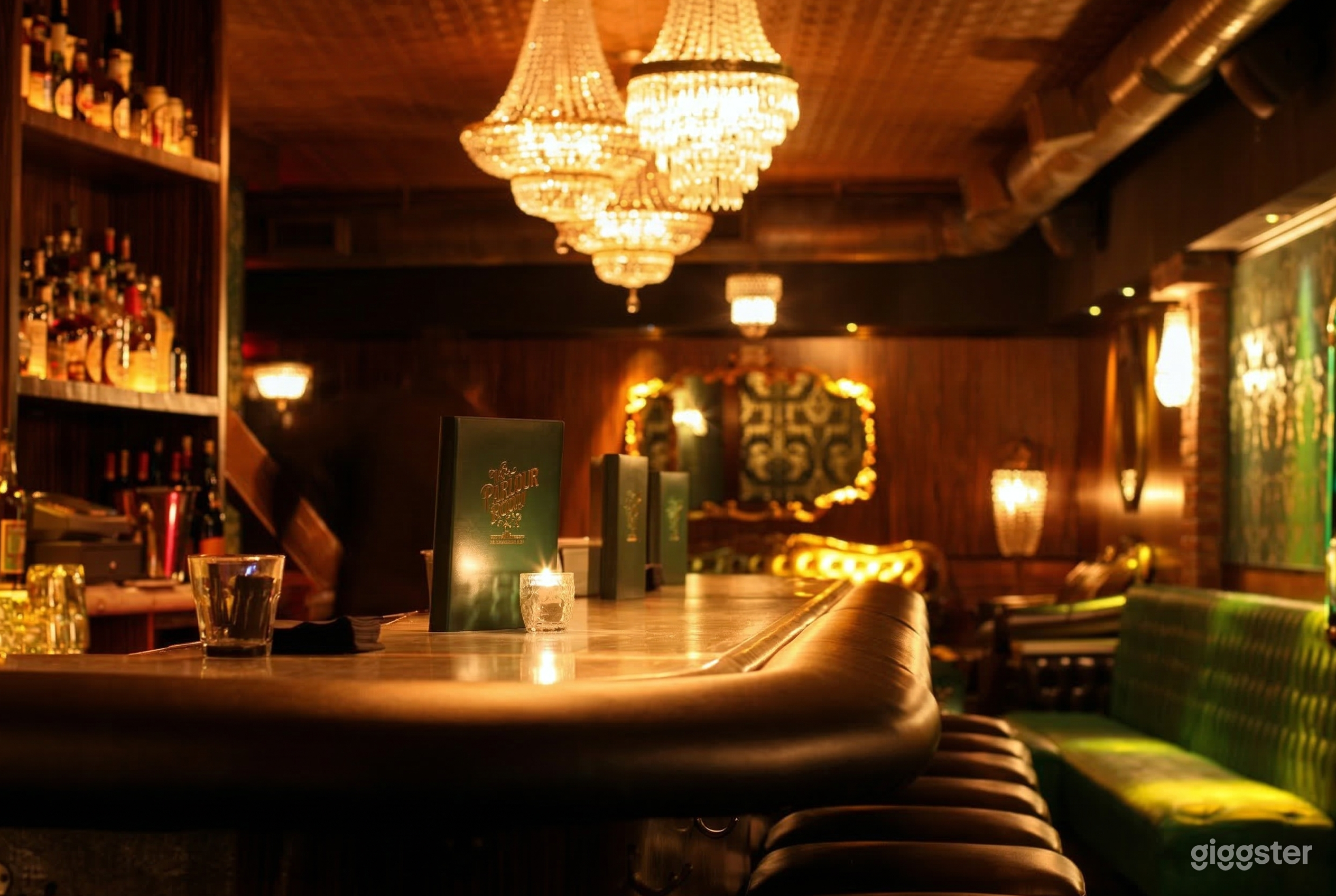 Close up of a shiny wood bar surface with chandeliers directly overhead and bar stools alongside.