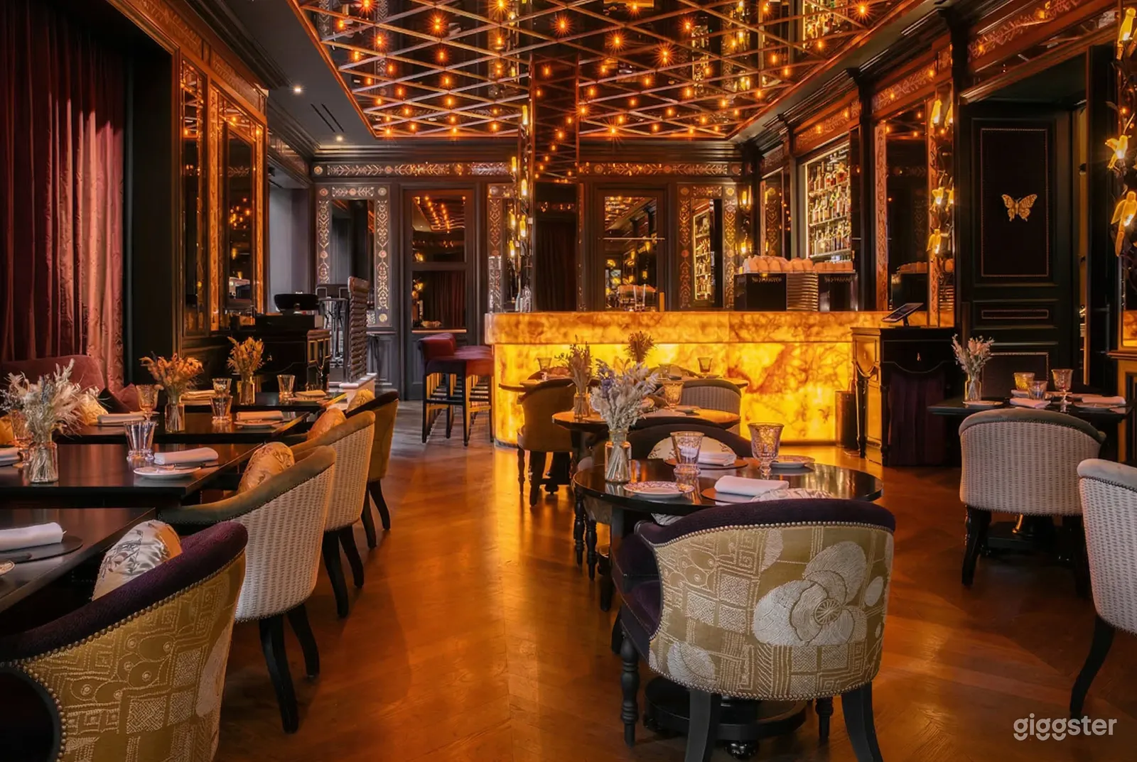 A warm and ornately decorated restaurant with curved traditional seating around tables set with flowers, glasses and plates.