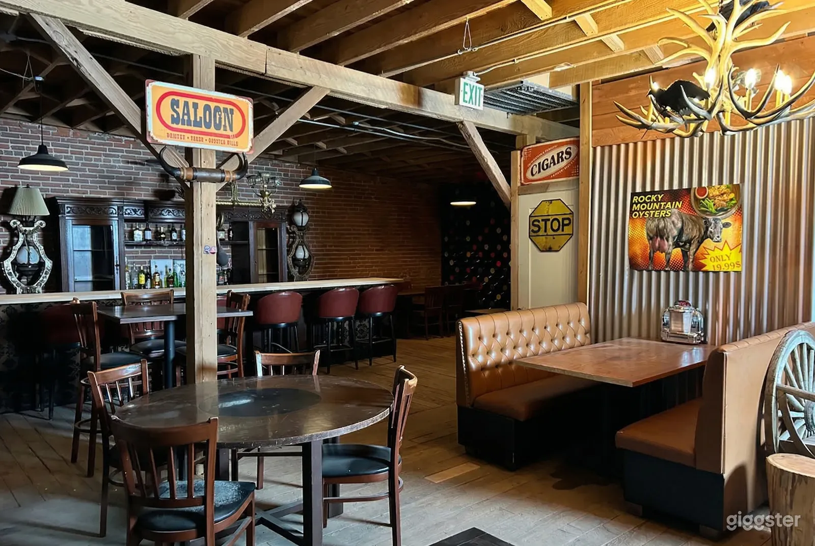 A room is styled similar to a saloon with a booth, table and chairs, and chairs lining a brick walled bar.