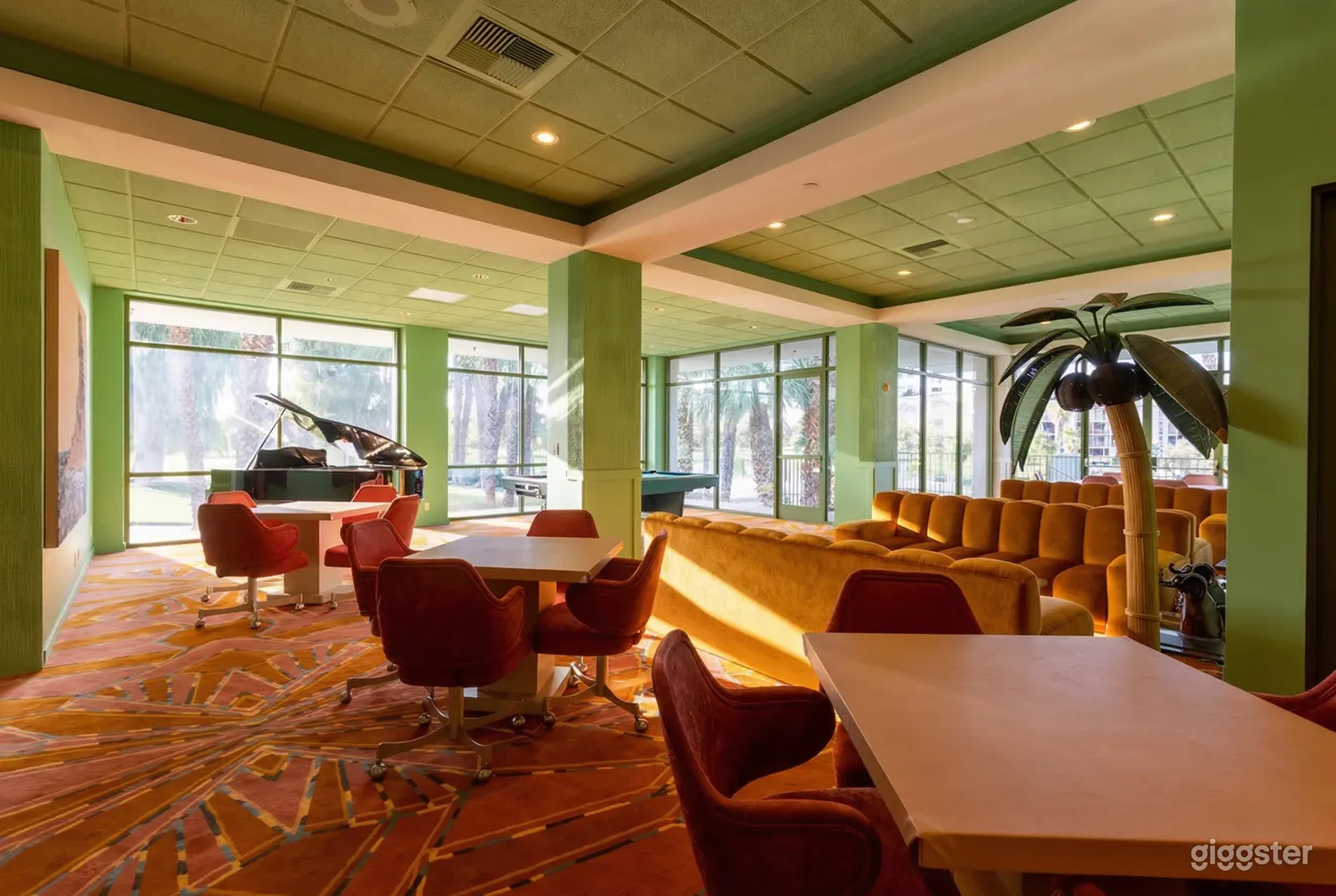 A room with a green ceiling and windowed walls contains seating, tables, and a grand piano.
